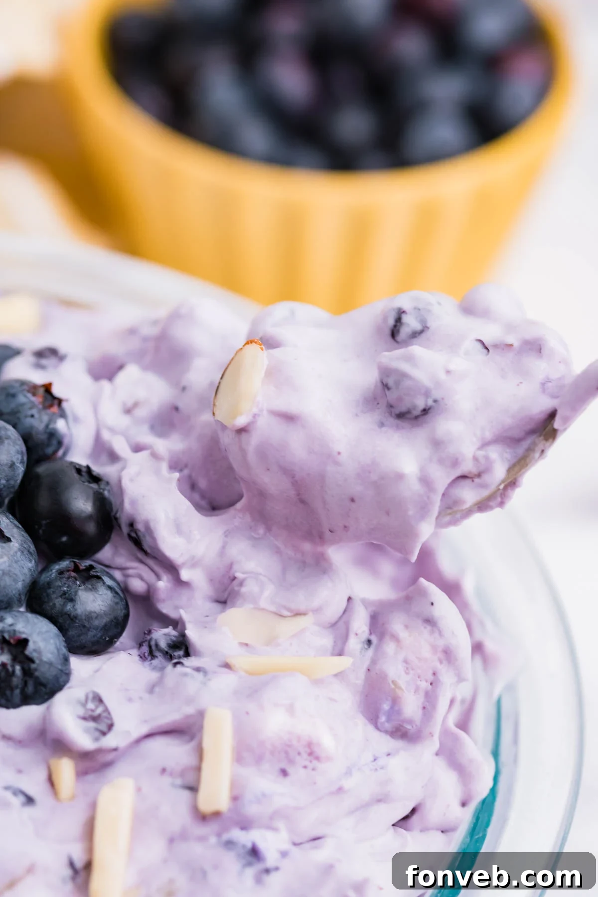 Blueberry Fluff Salad in a clear glass bowl with a spoon lifting it out