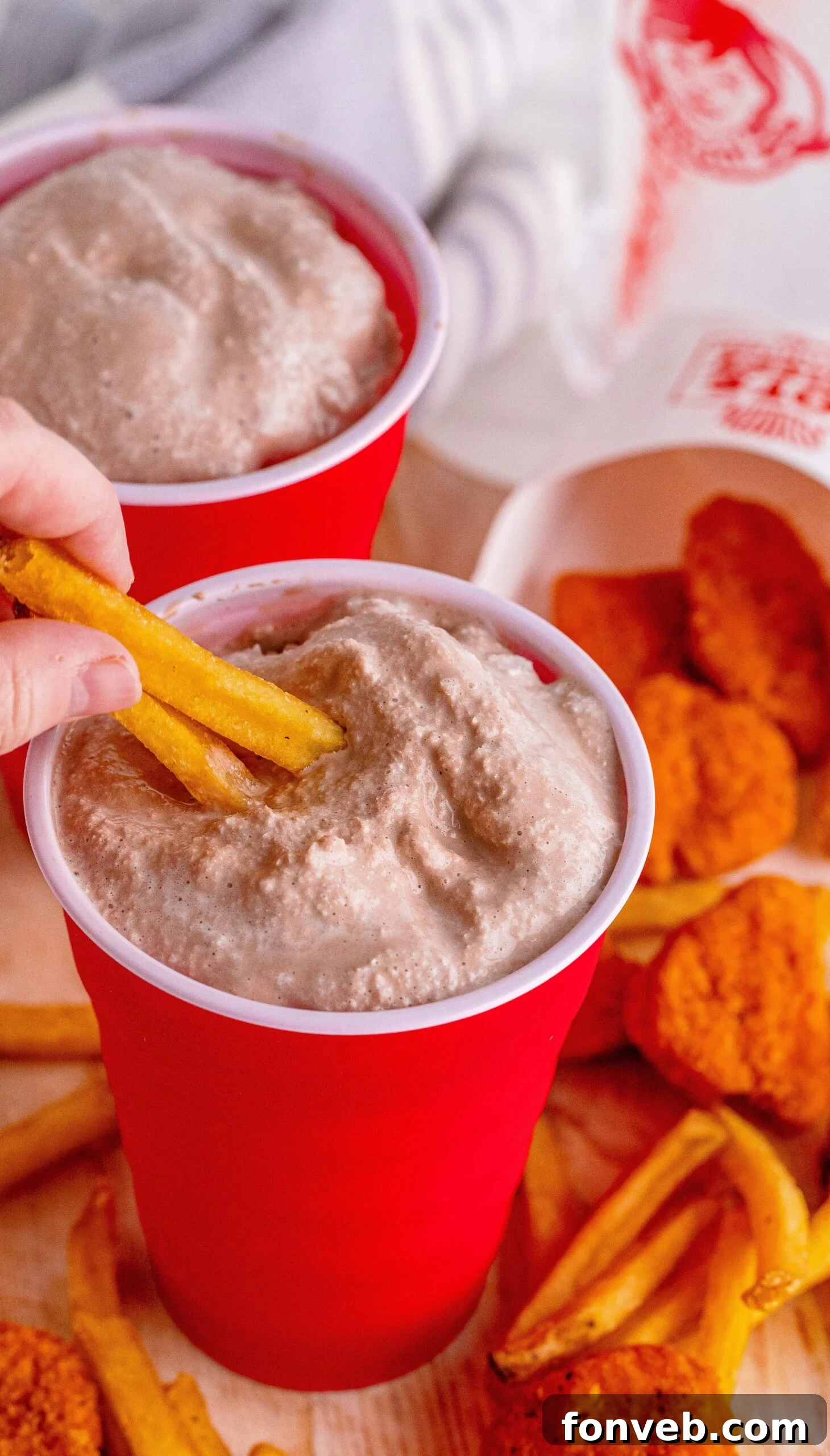 Hand dipping a crispy french fry into a homemade Wendy's Frosty in a red solo cup
