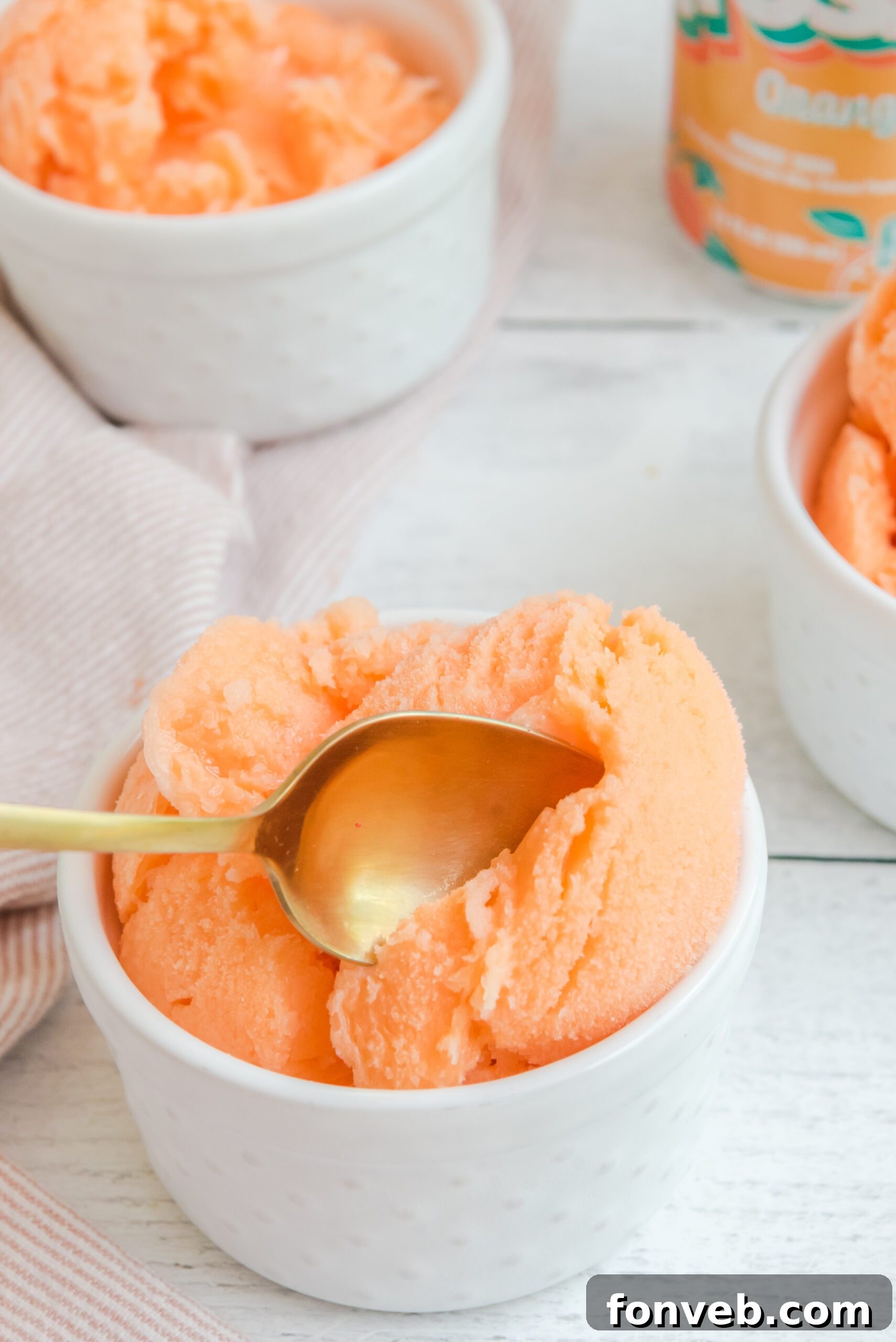 A gold spoon digging into Orange Crush Sherbet in a white bowl, demonstrating its scoopable consistency