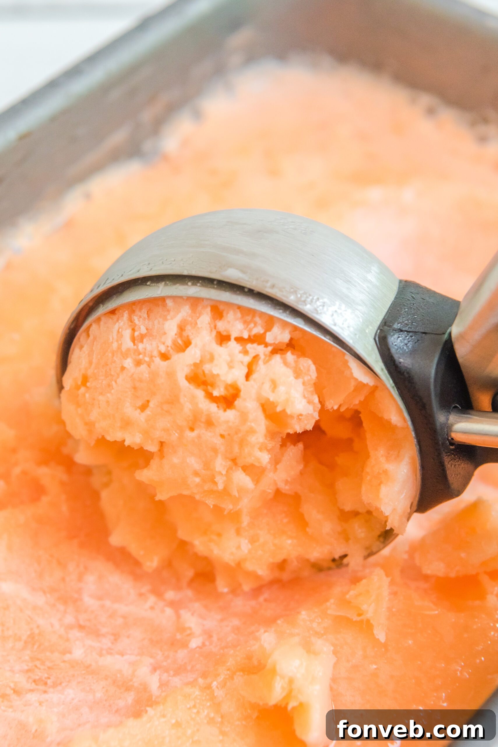Orange Crush Sherbet resting in a steel loaf pan, with an ice cream scooper poised to serve, illustrating its firm but scoopable texture