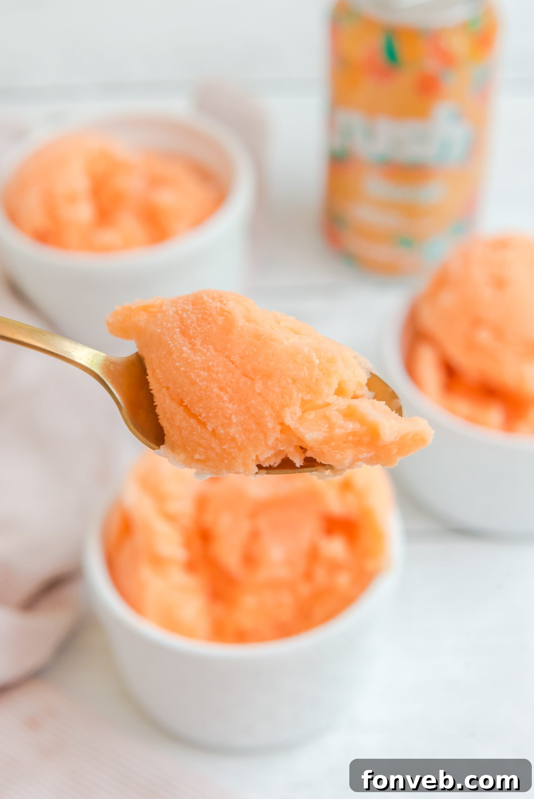 A spoonful of Orange Crush Sherbet being lifted from a white bowl, highlighting its perfect frozen consistency