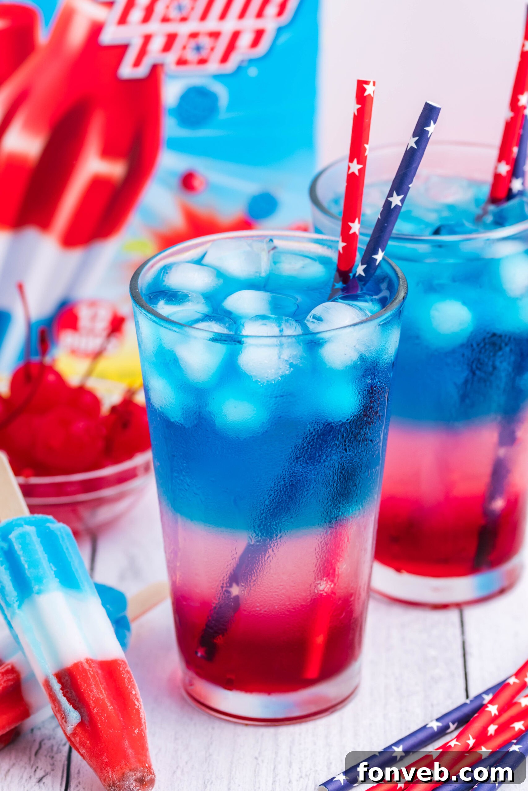 Bomb Pop Cocktail Drink in a clear glass with a blue & red straw with bomb pop ice cream box in the background