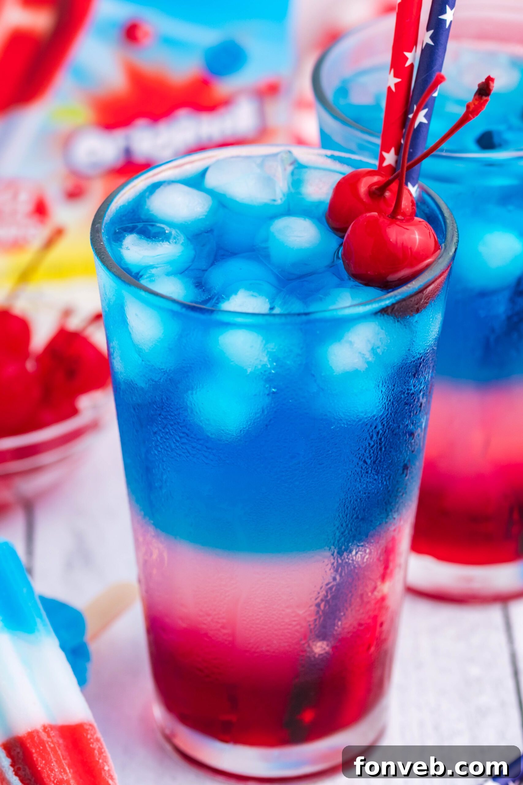 Bomb Pop Cocktail Drink in a clear glass with a blue & red straw with cherries floating