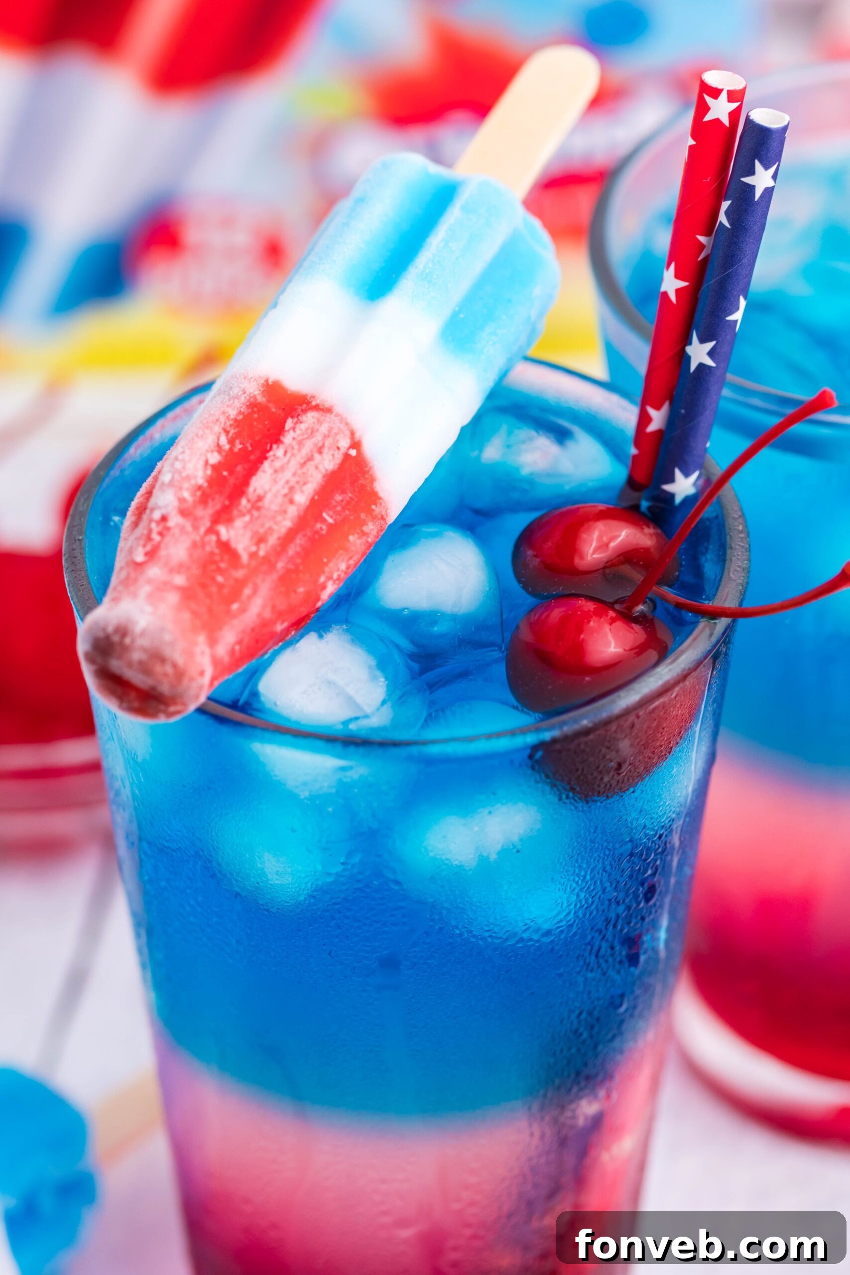 Bomb Pop Cocktail Drink in a clear glass with a blue & red straw with cherries floating