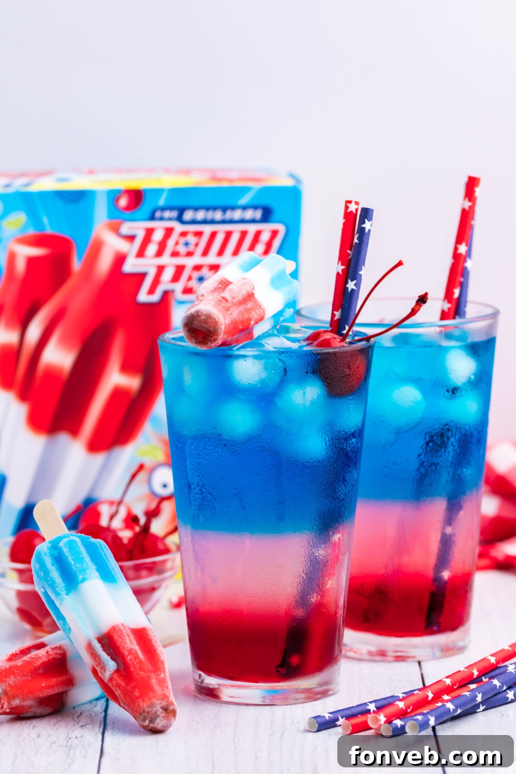 Bomb Pop Cocktail Drink in a clear glass with a blue & red straw with cherries floating far away shot