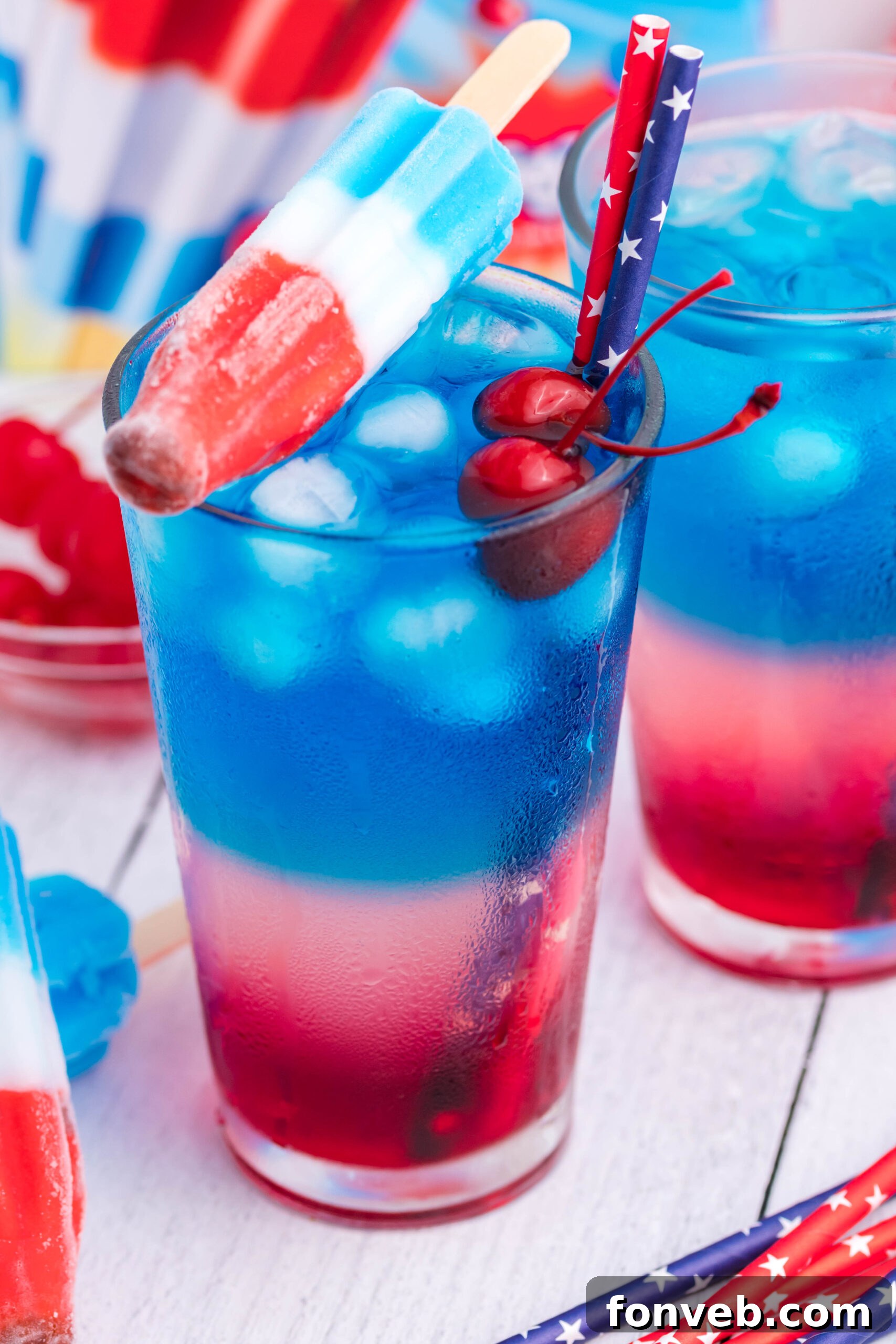 Bomb Pop Cocktail Drink in a clear glass with a blue & red straw with cherries floating