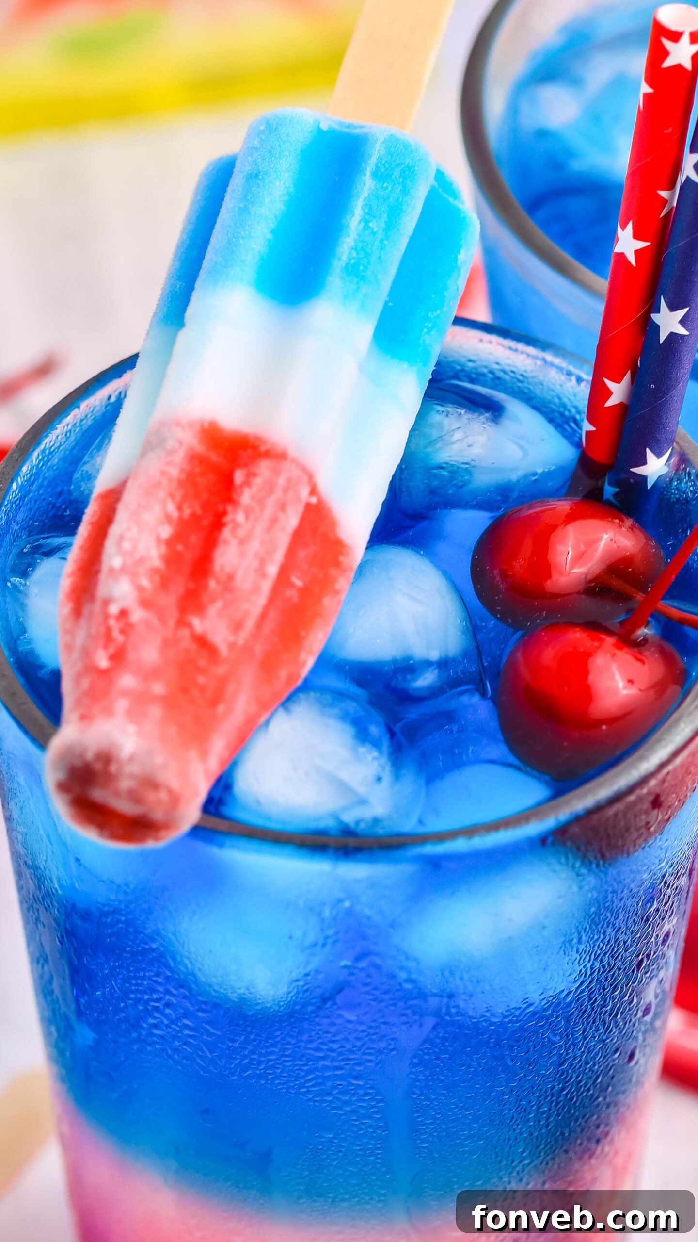 Bomb Pop Cocktail Drink in a clear glass with a blue & red straw with cherries floating up close