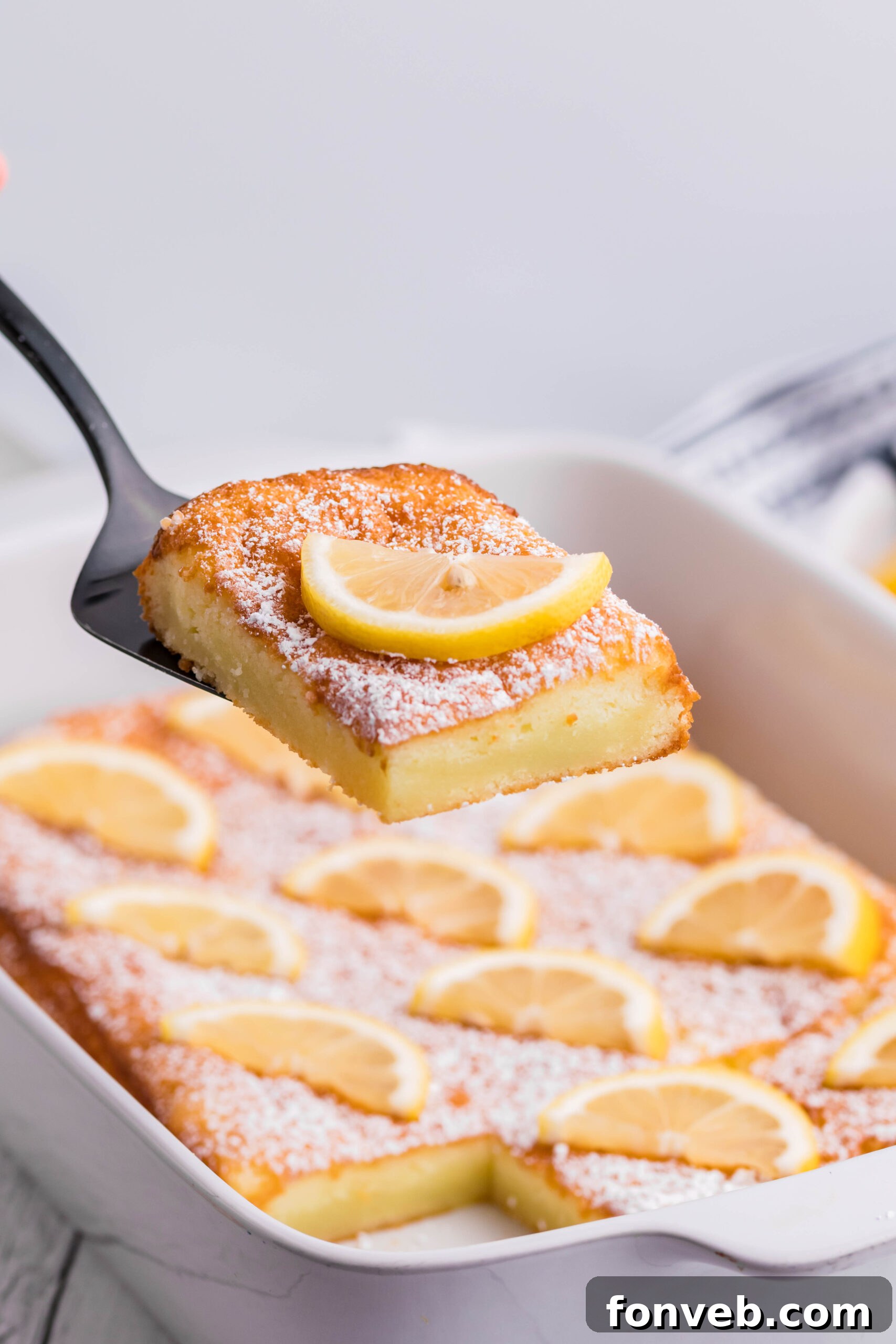 2 Ingredient Lemon Bars in a white baking pan with a slice being lifted on a spatula