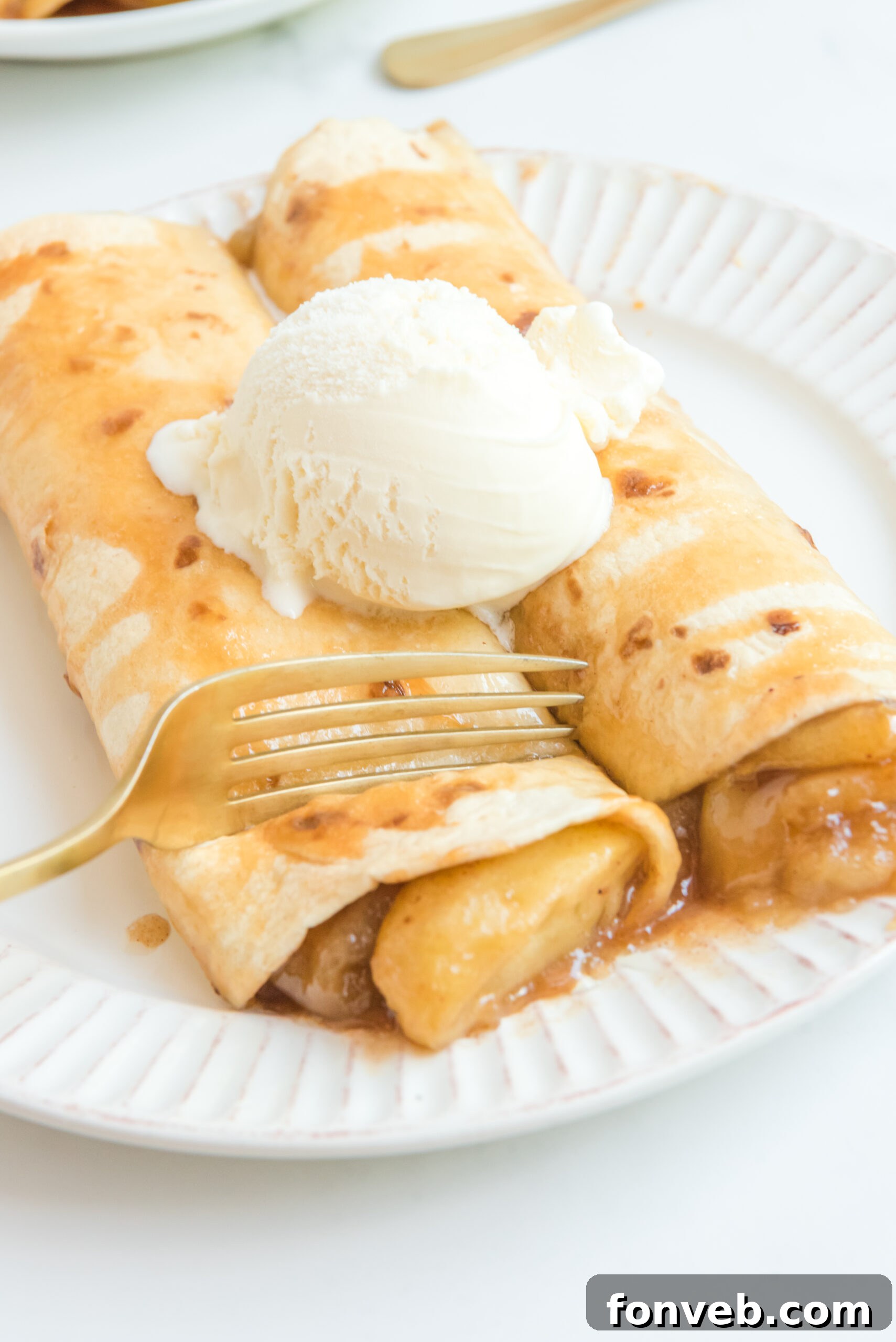 Apple Pie Enchiladas topped with vanilla ice cream with a fork slicing into it