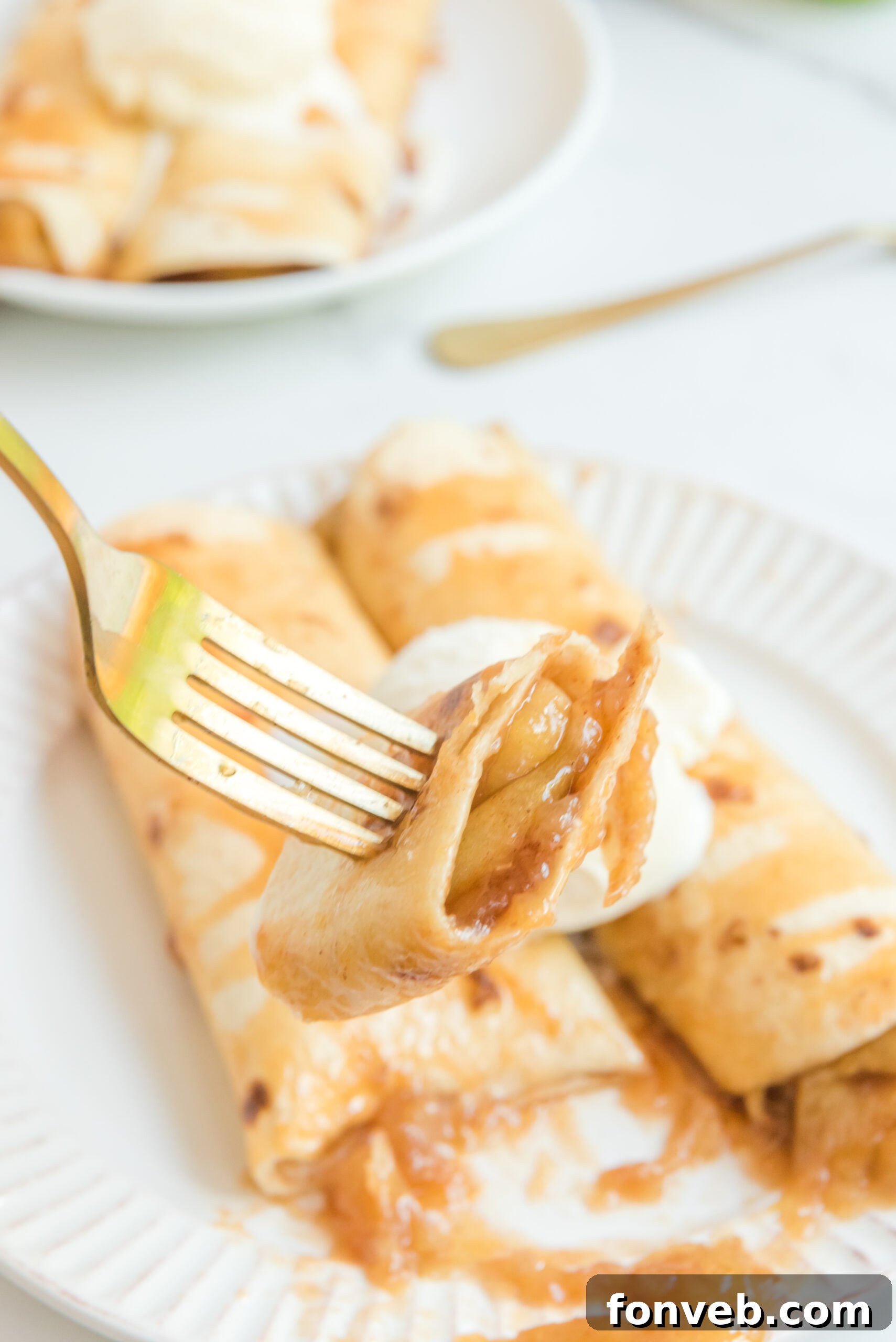 Apple Pie Enchiladas topped with vanilla ice cream with a bite being lifted on a fork
