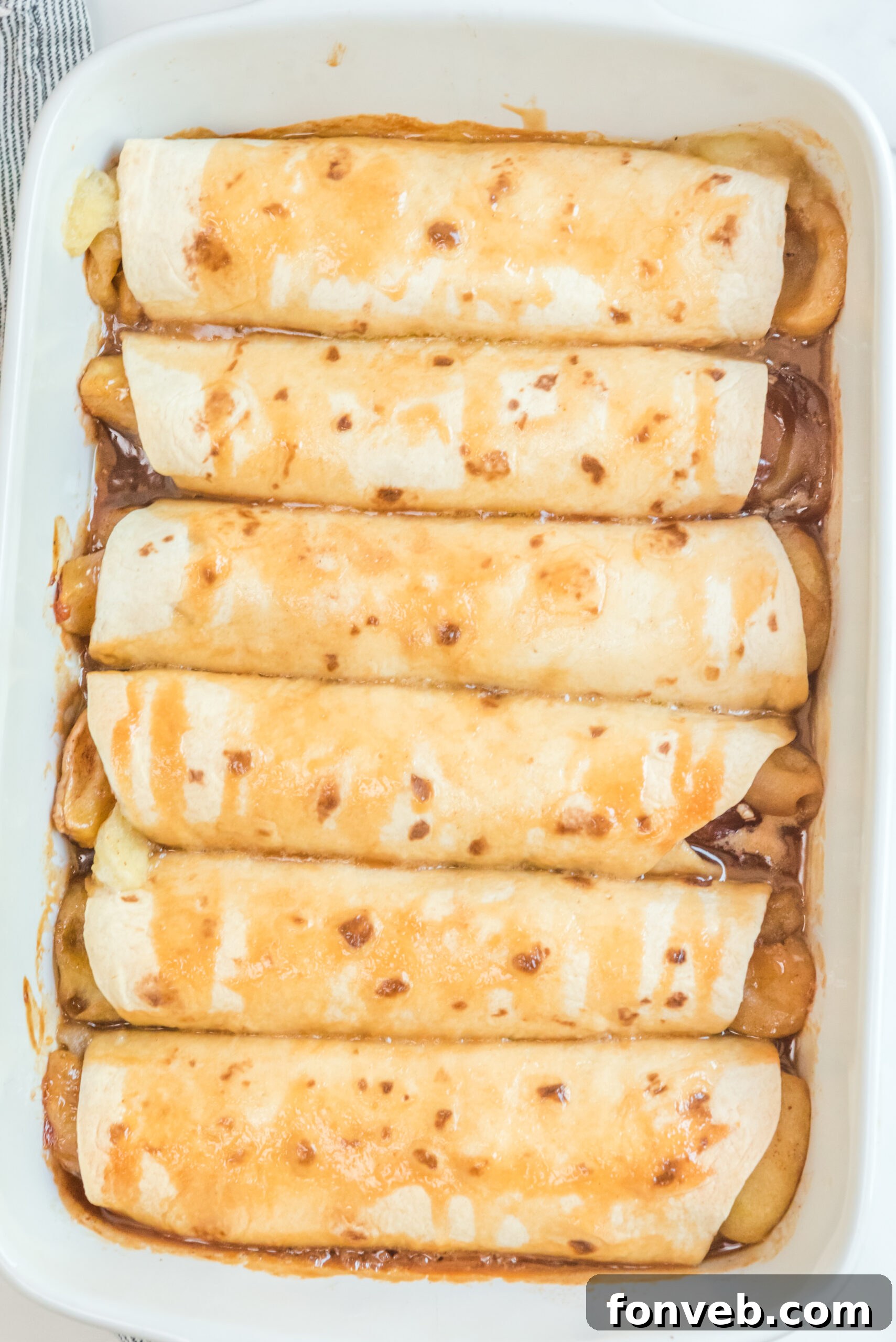 Apple Pie Enchiladas topped with caramel sauce in a white baking dish overhead shot