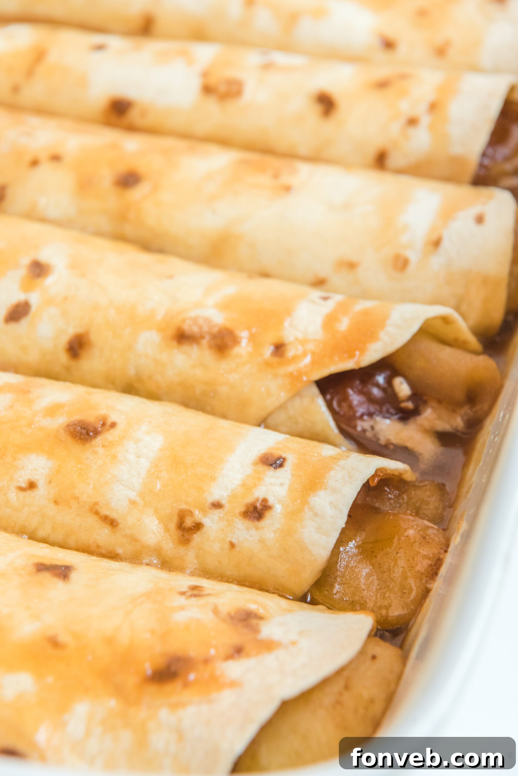 Apple Pie Enchiladas topped with caramel sauce in a white baking dish