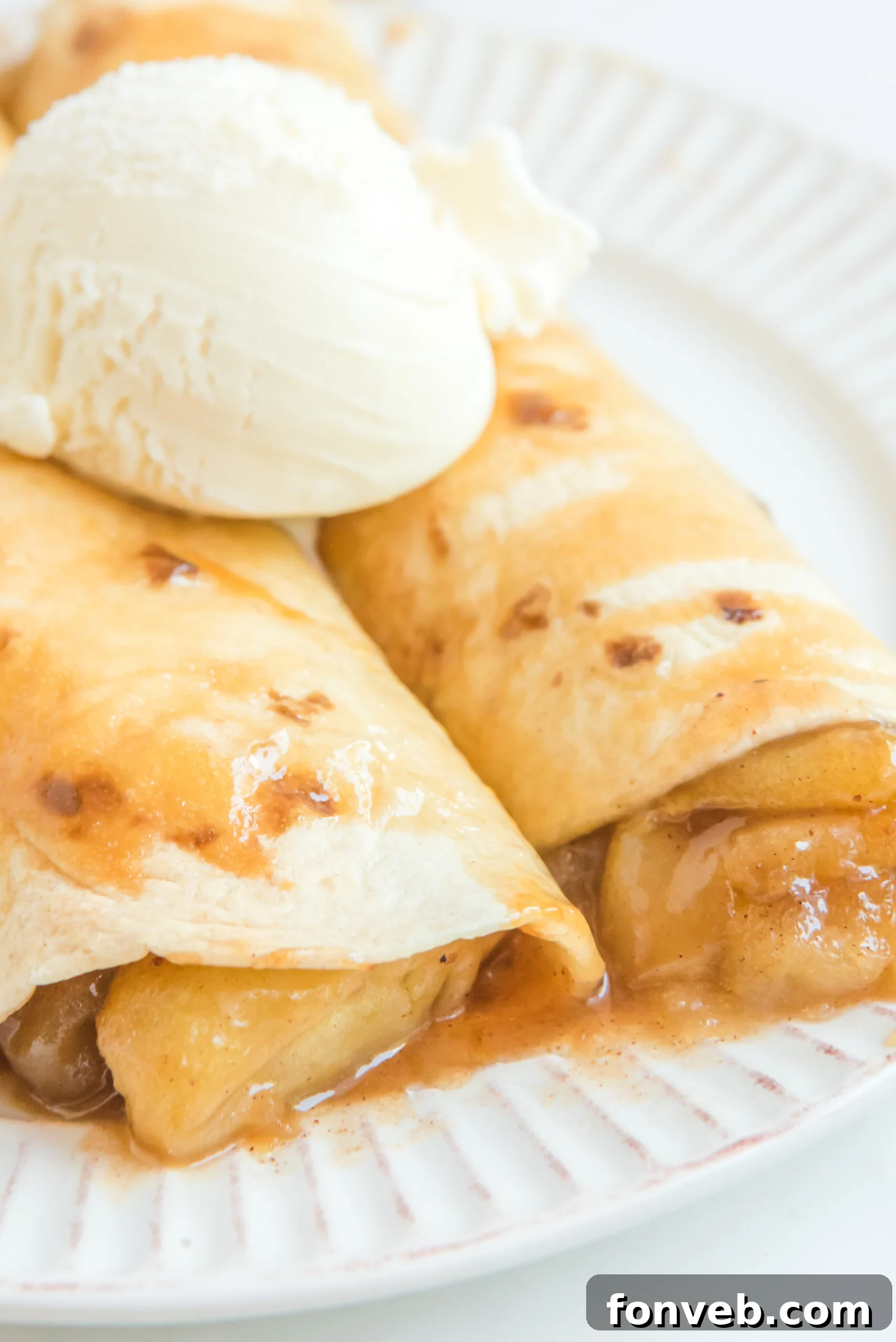 Apple Pie Enchiladas topped with vanilla ice cream showing apples dripping out