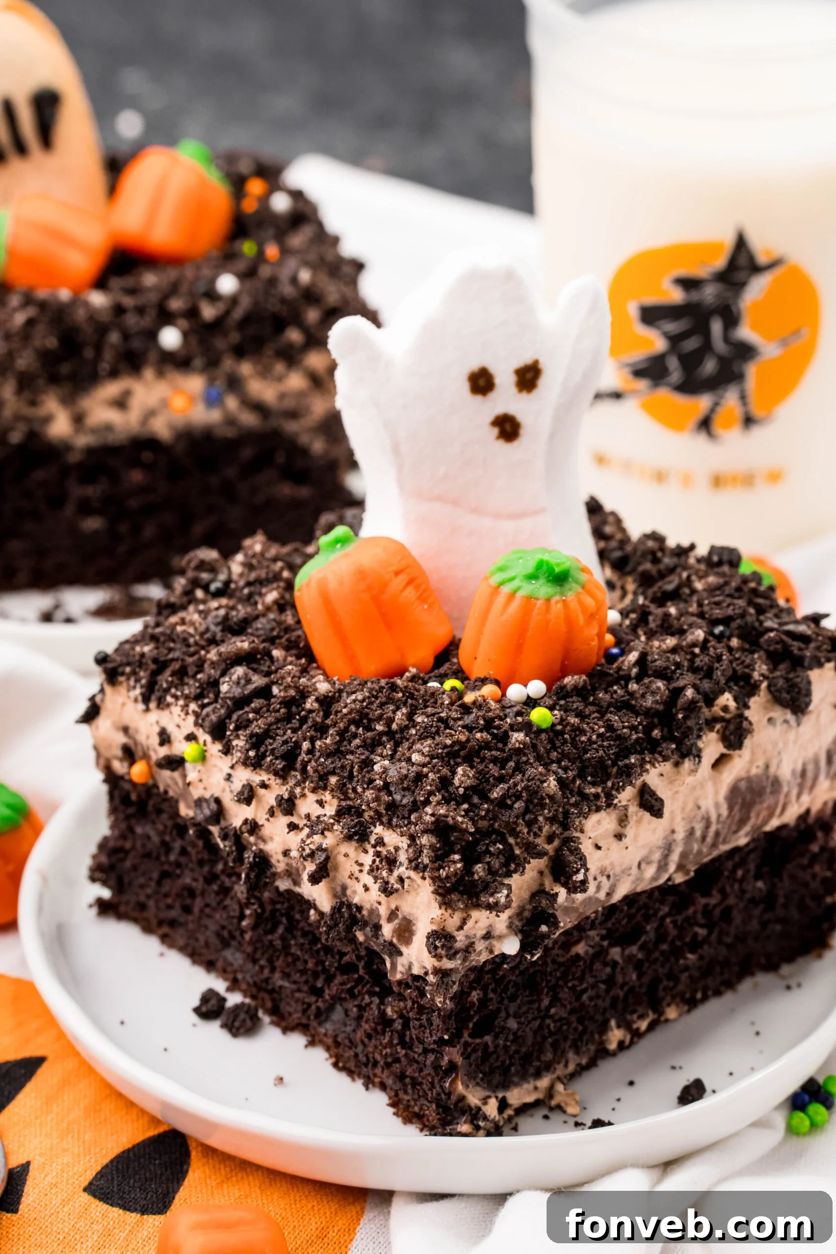 A perfectly sliced Halloween Dirt Cake revealing its luscious layers, served on a crisp white plate, topped with a charming ghost marshmallow peep and scattered candy pumpkins.