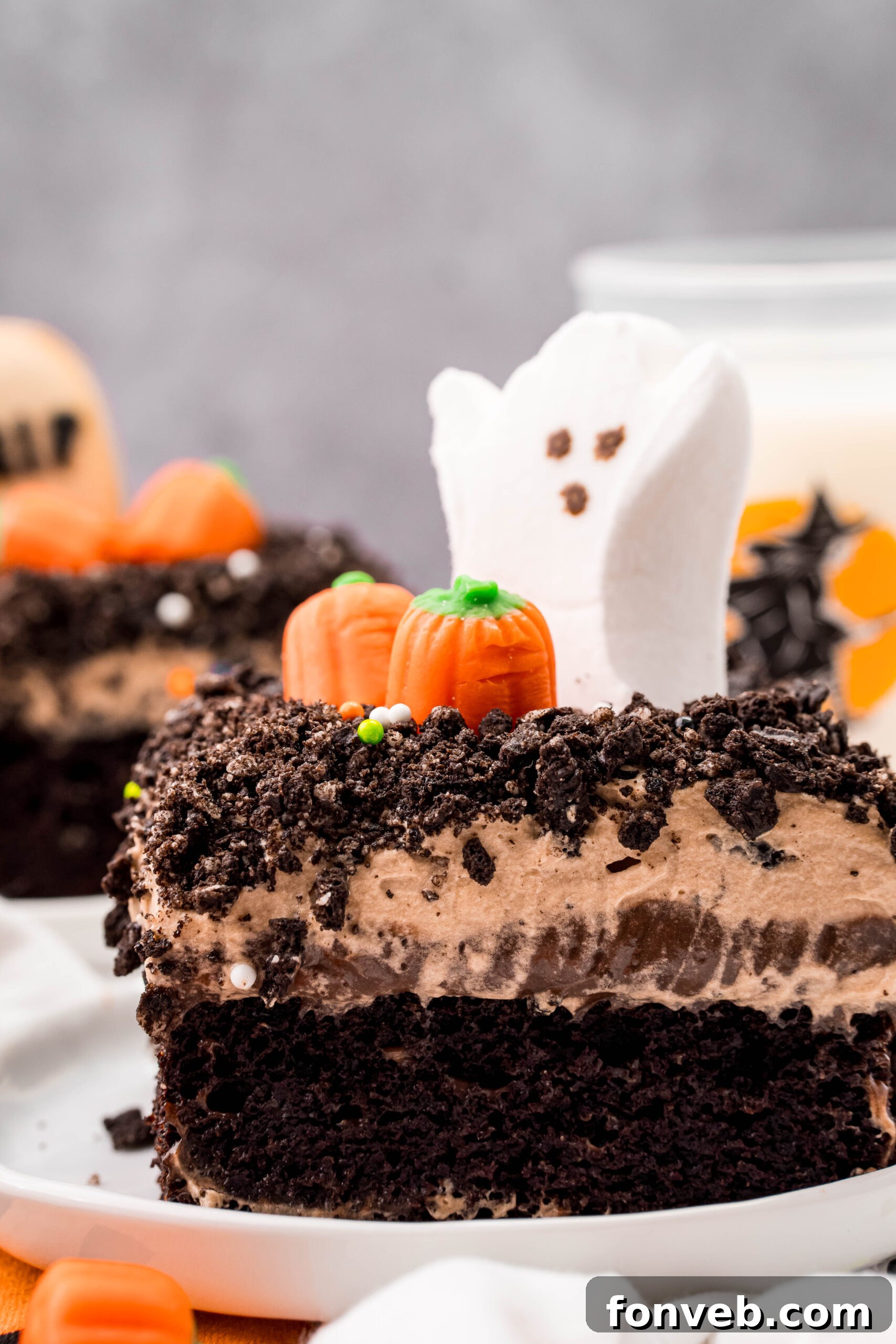 A delicious slice of Halloween Dirt Cake on a white plate, prominently featuring a cute ghost marshmallow peep and a sprinkling of Oreo crumbles, ready to be devoured.
