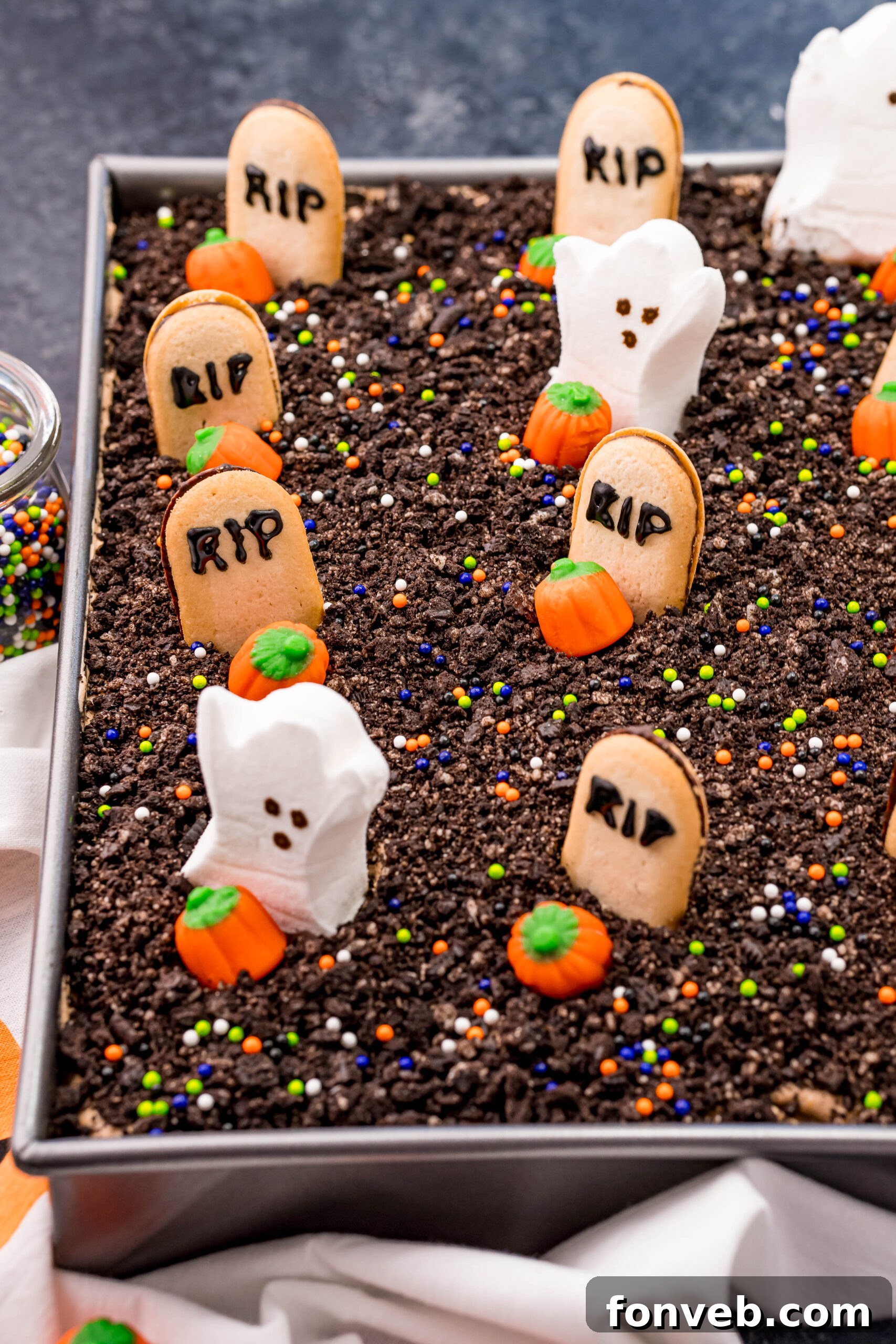An uncut Halloween Dirt Cake, magnificently decorated with an assortment of spooky toppings, nestled in a shimmering silver baking pan, ready for slicing.