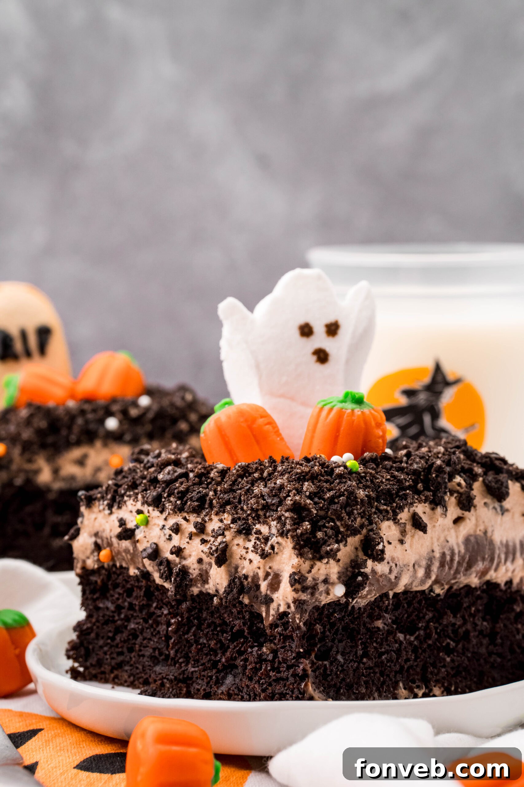 A serving of Halloween Dirt Cake on a white plate, with a refreshing glass of milk elegantly blurred in the background, creating a cozy and inviting scene.