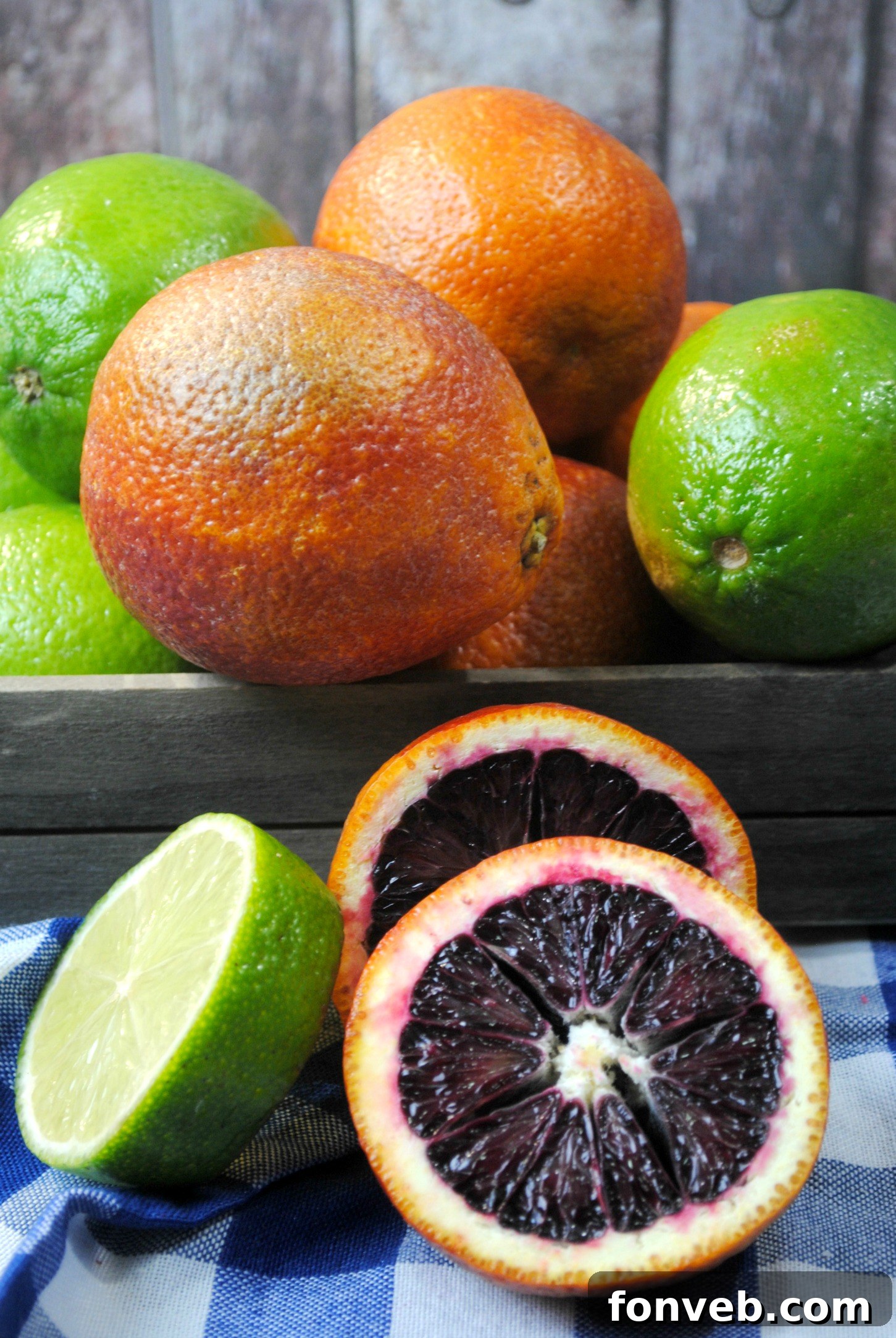 A hand gently holds a glass of Blood Orange Margarita with a sparkling sugared rim, set against a blurred background of a sunlit swimming pool.