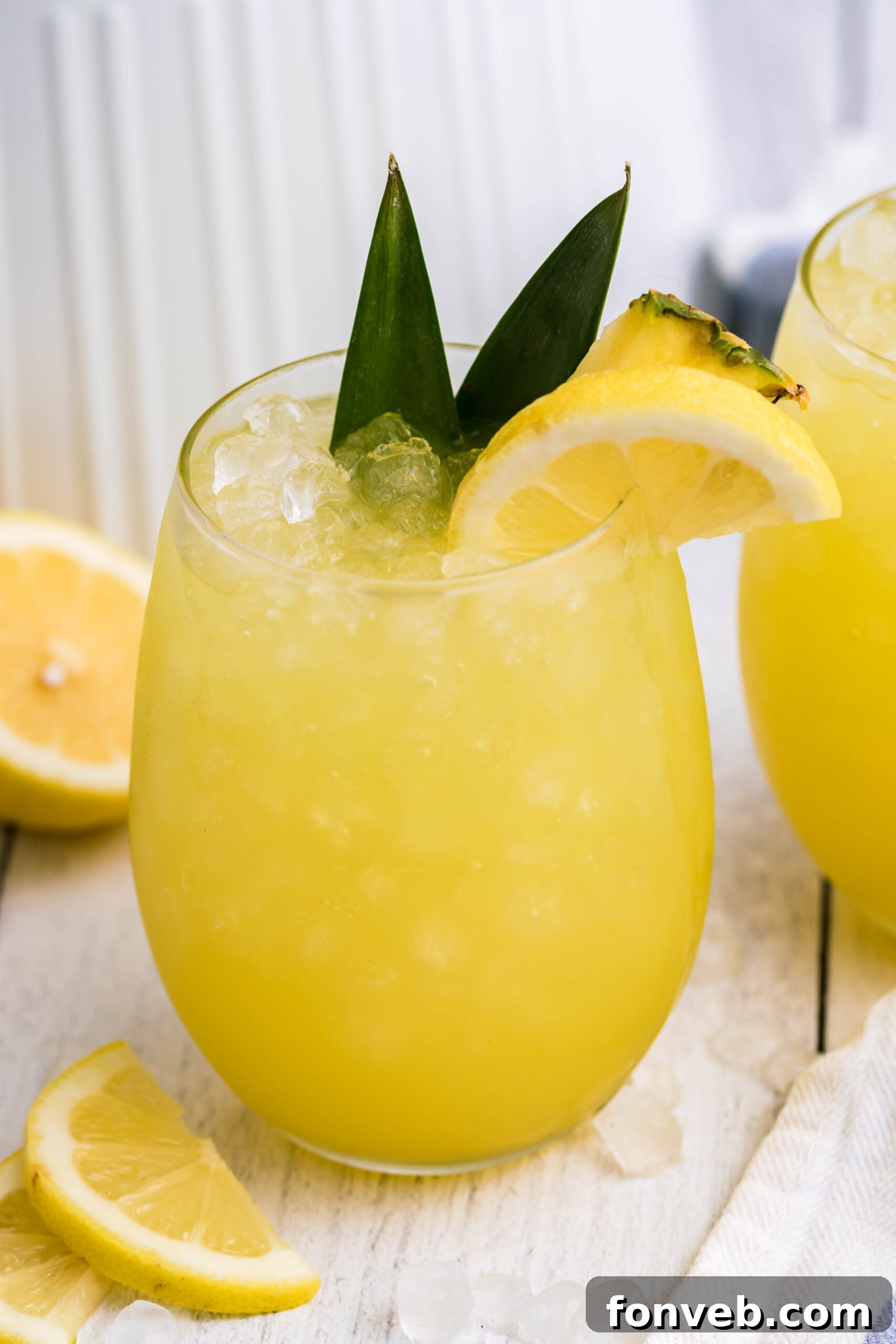 Pineapple Lemonade in a clear glass, garnished with fresh pineapple leaves and a lemon slice within the glass, highlighting its natural elements