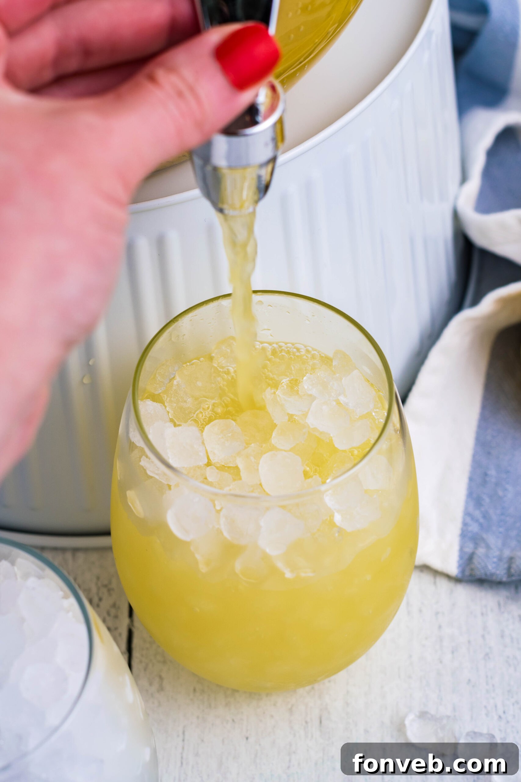 Pineapple Lemonade being carefully poured from a pitcher into a glass filled with crushed ice, creating a refreshing splash