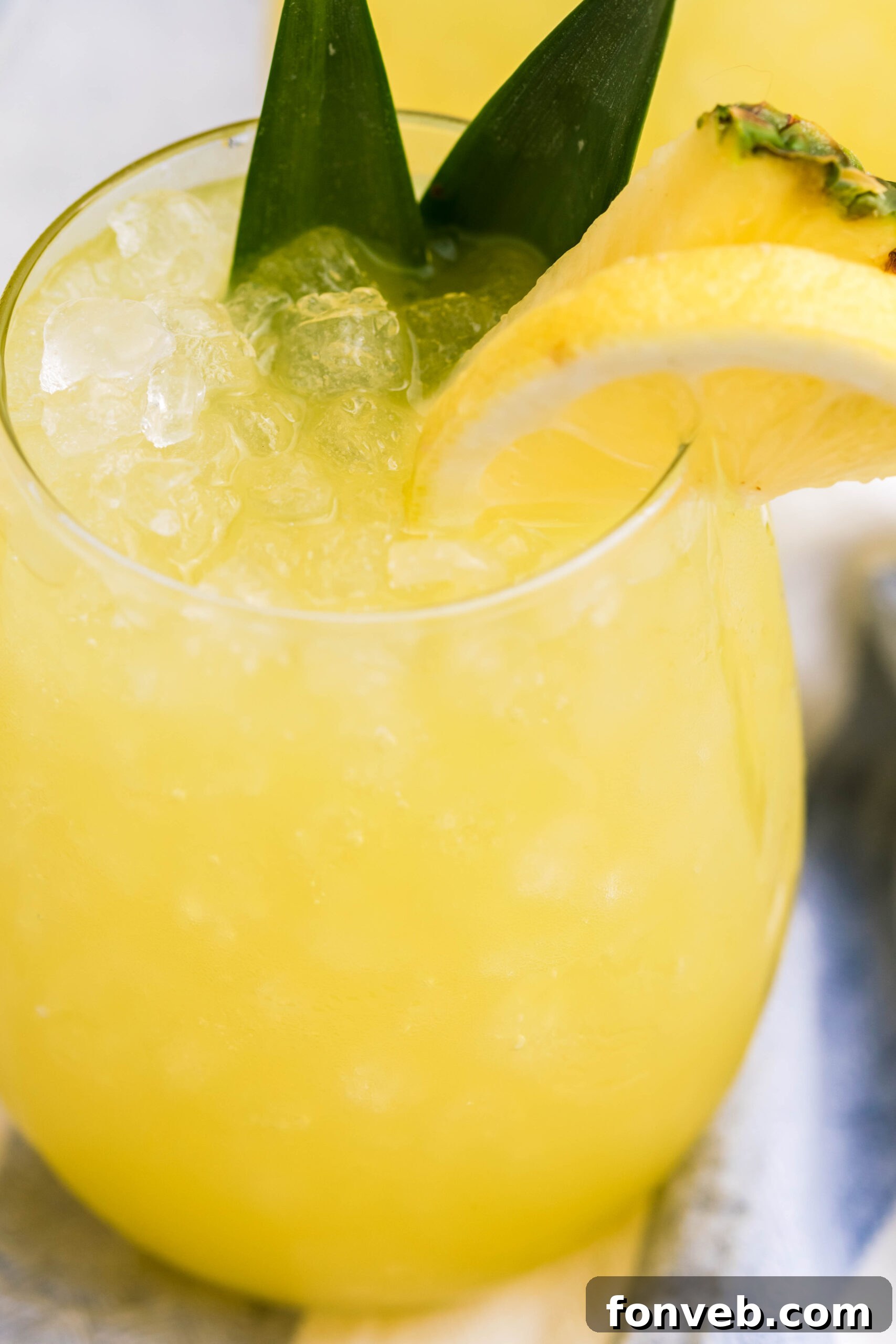 Close-up shot of Pineapple Lemonade in a clear glass, showing ice and vibrant yellow color, inviting a sip
