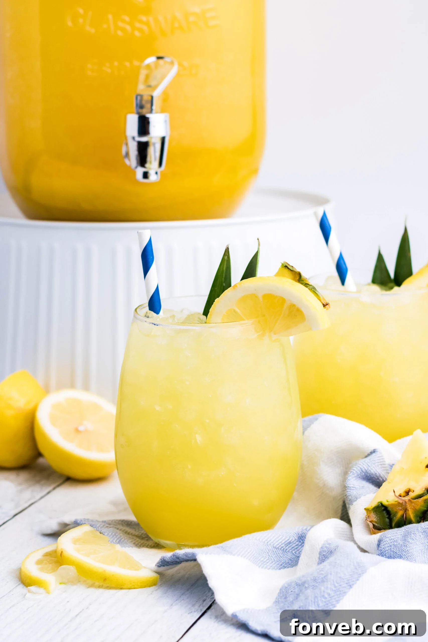 Pineapple Lemonade in a clear glass with ice, a blue striped straw, and fresh lemon slices, captured from an eye-level perspective