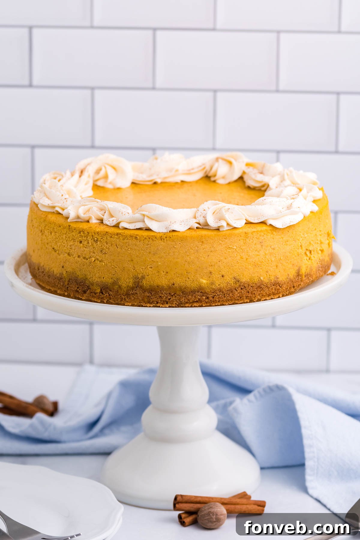 A wider shot of the Pumpkin Cheesecake sitting elegantly on a white cake stand, highlighting its rich color