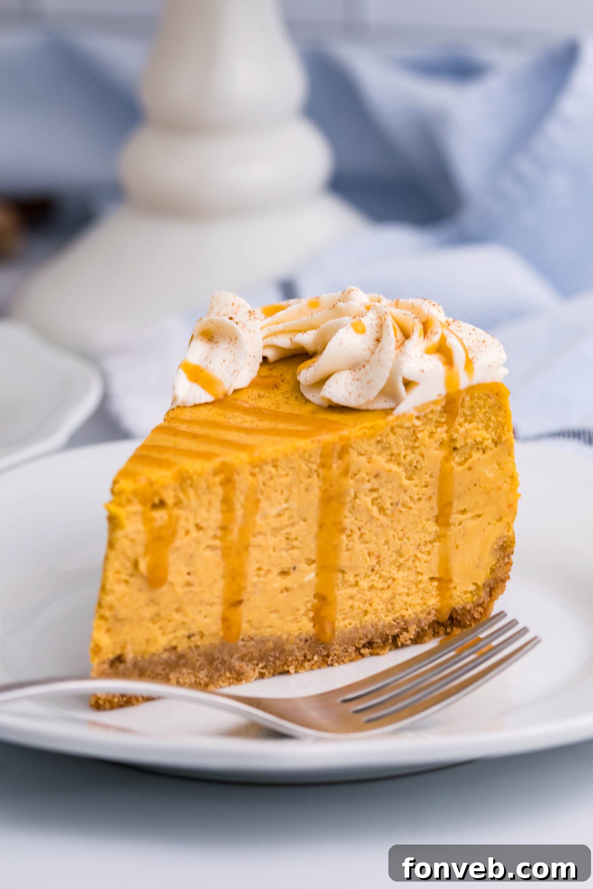 A slice of Pumpkin Cheesecake on a white plate with a fork placed beside it, inviting a taste