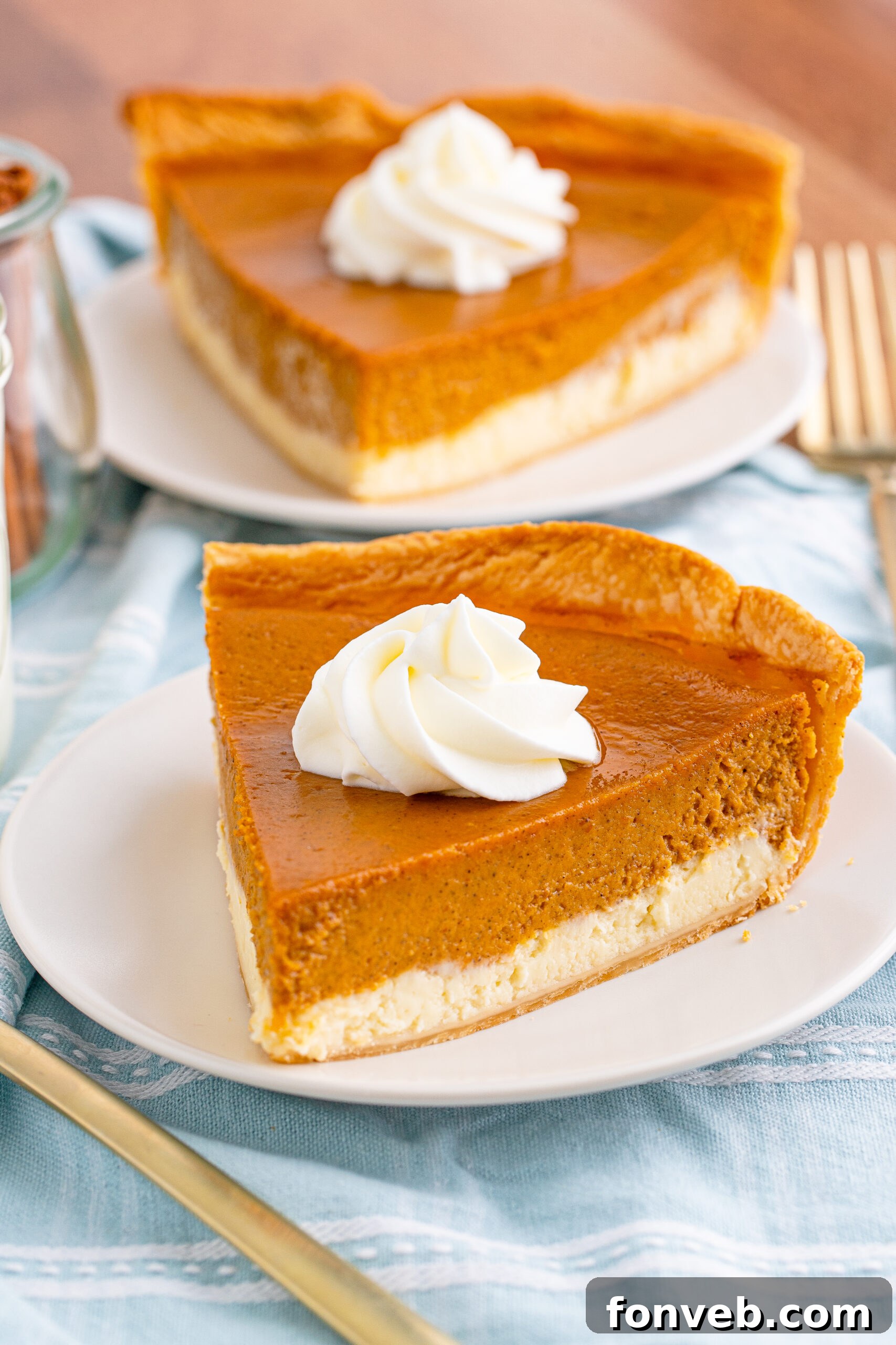 A perfectly sliced Pumpkin Pie Cheesecake on a white plate, showcasing distinct layers of creamy cheesecake and spiced pumpkin