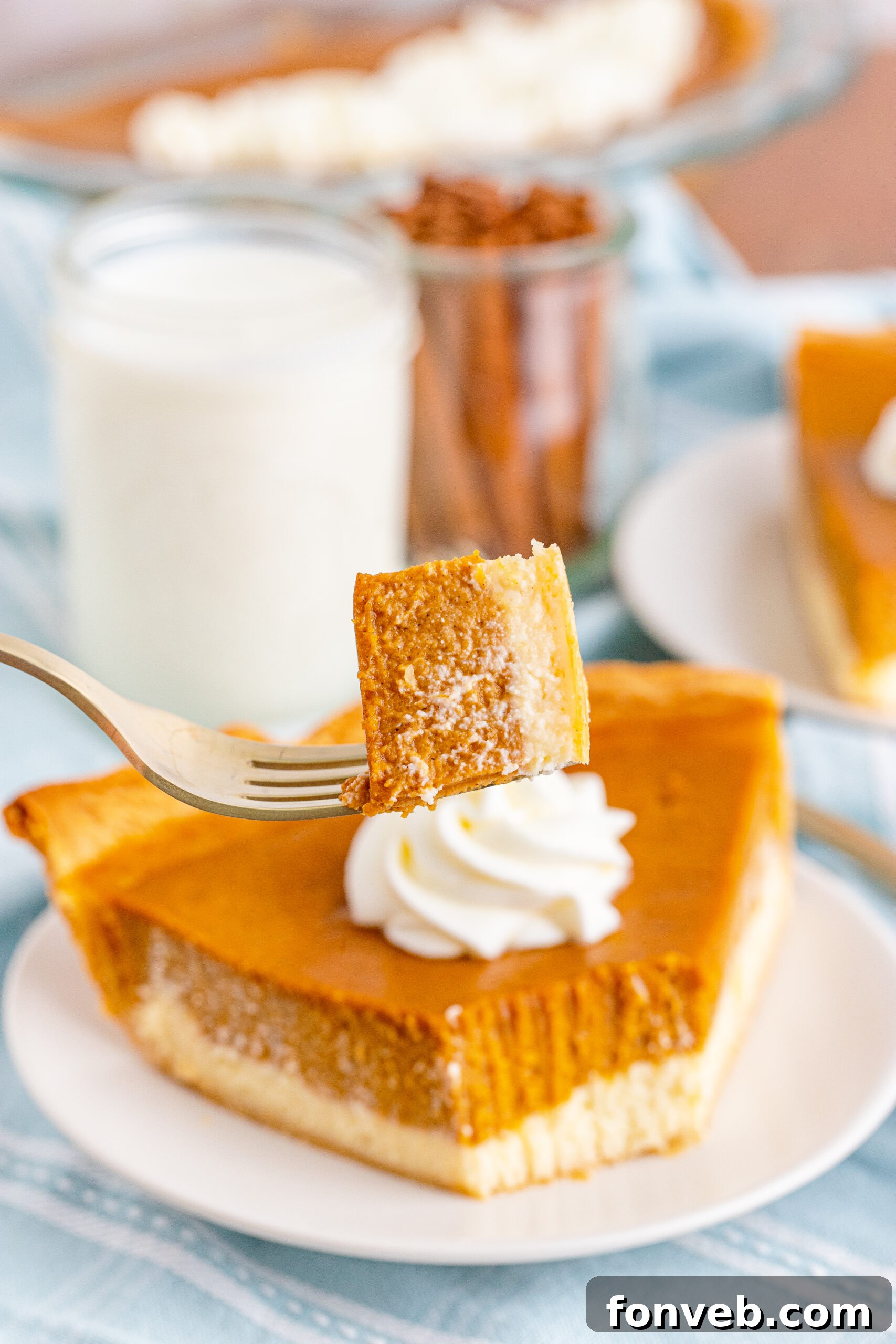 A slice of Pumpkin Pie Cheesecake on a white plate with a fork lifting a bite, showing the texture