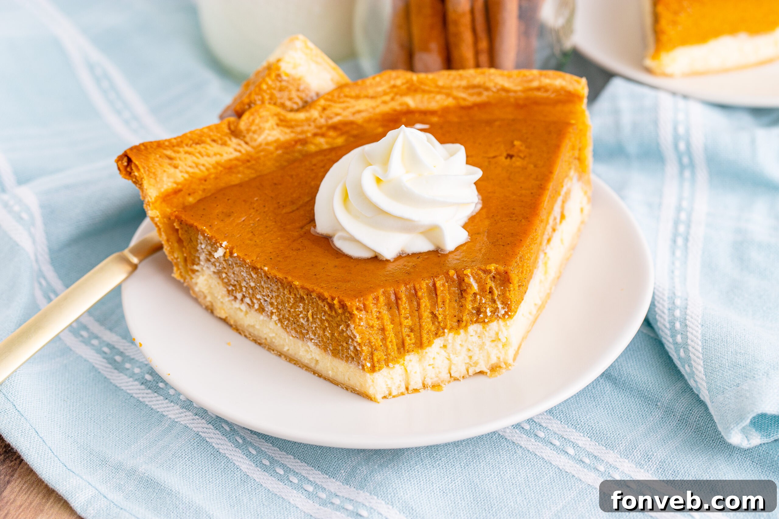 A slice of Pumpkin Pie Cheesecake on a white plate topped with a generous swirl of whipped cream