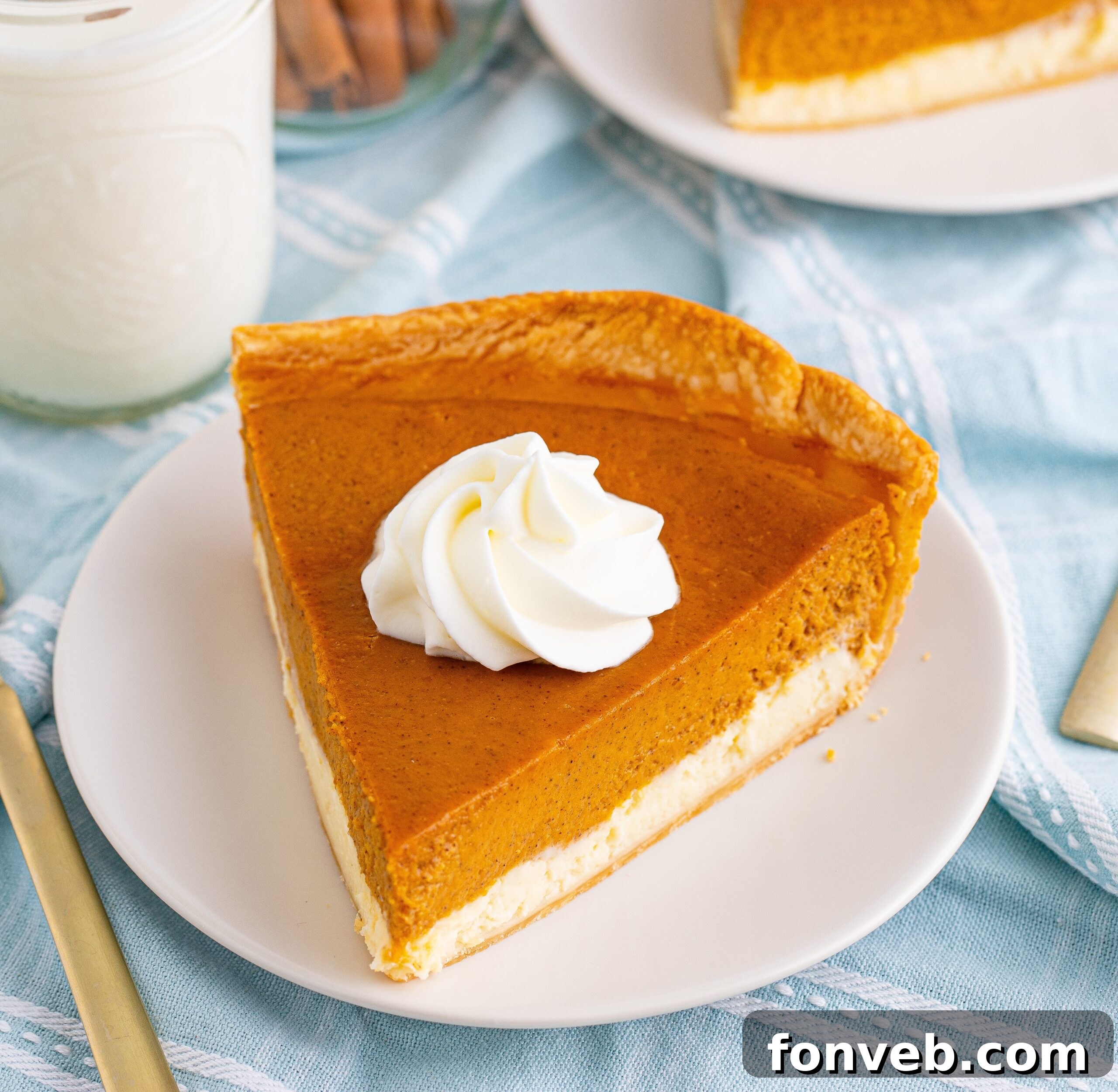 A slice of Pumpkin Pie Cheesecake on a white plate with a glass of milk beside it