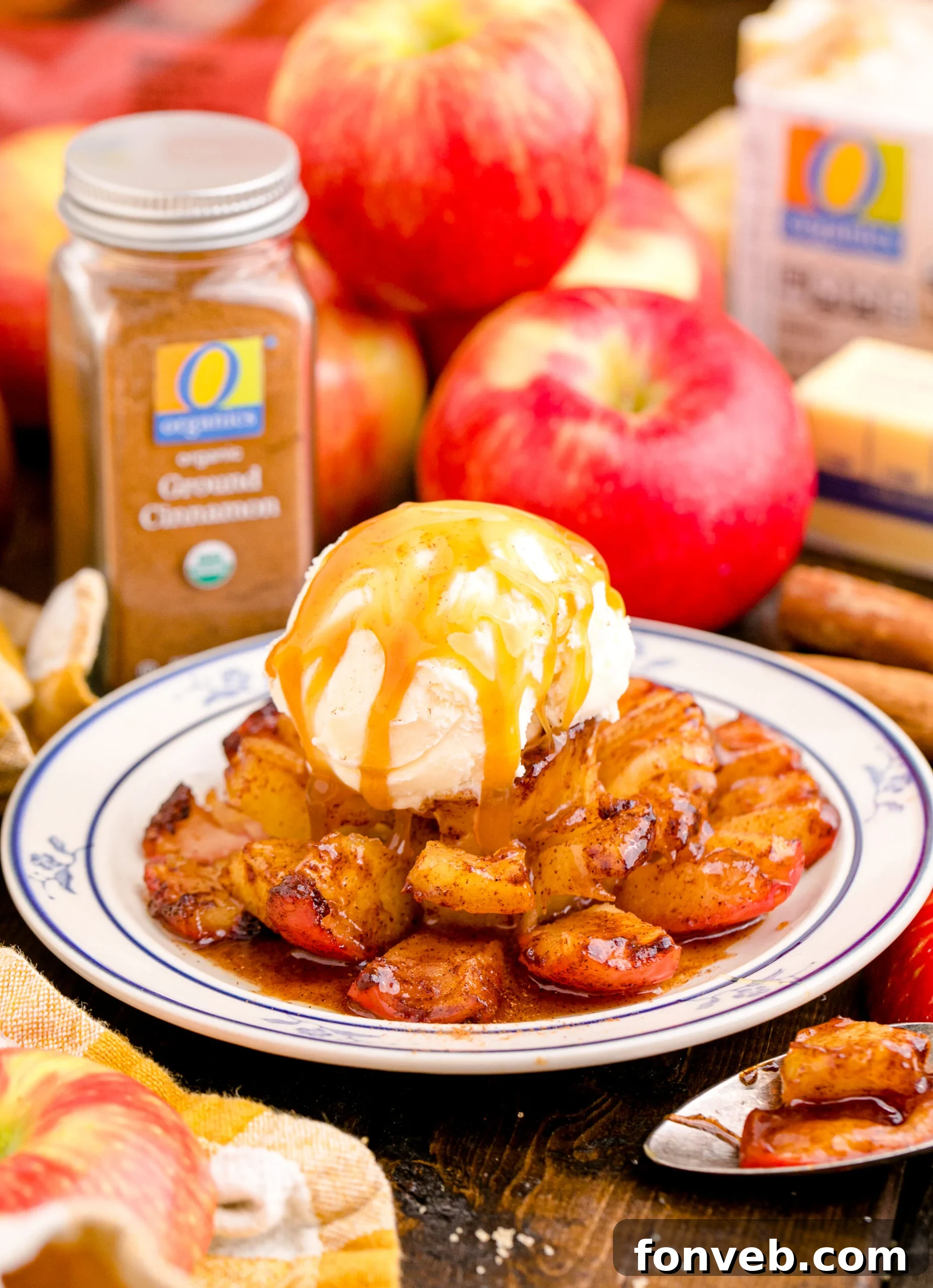 Oven Baked Bloomin Apples on a white plate topped with ice cream and caramel sauce with apples and a jar of cinnamon in the background