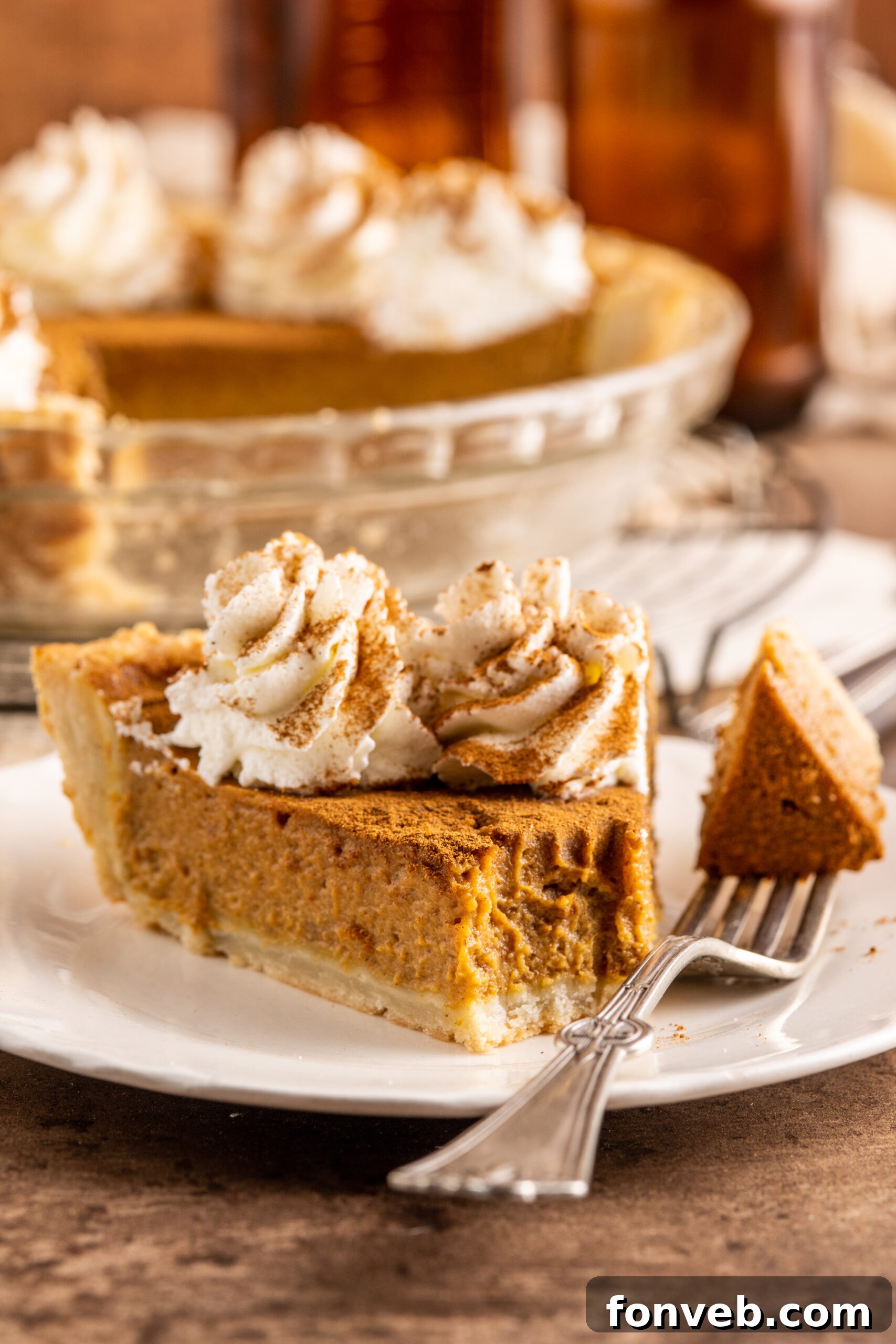 Velvet Pumpkin Dream Pie 2 A perfectly golden-brown slice of Pumpkin Custard Pie resting on a white plate, with a fork lifting a bite, showcasing its creamy texture.