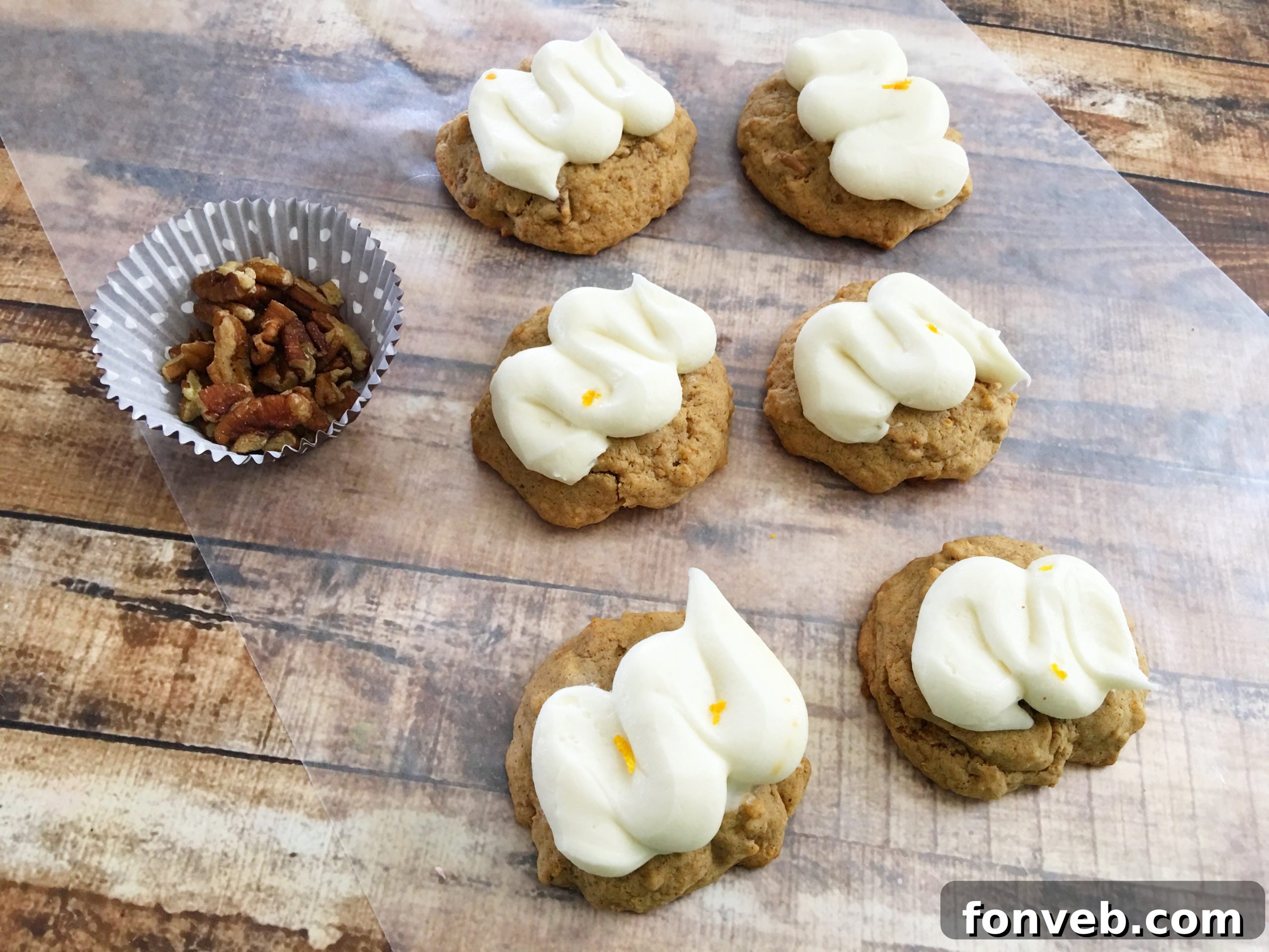 Carrot cake cookies generously topped with orange cream cheese frosting and a sprinkle of pecans