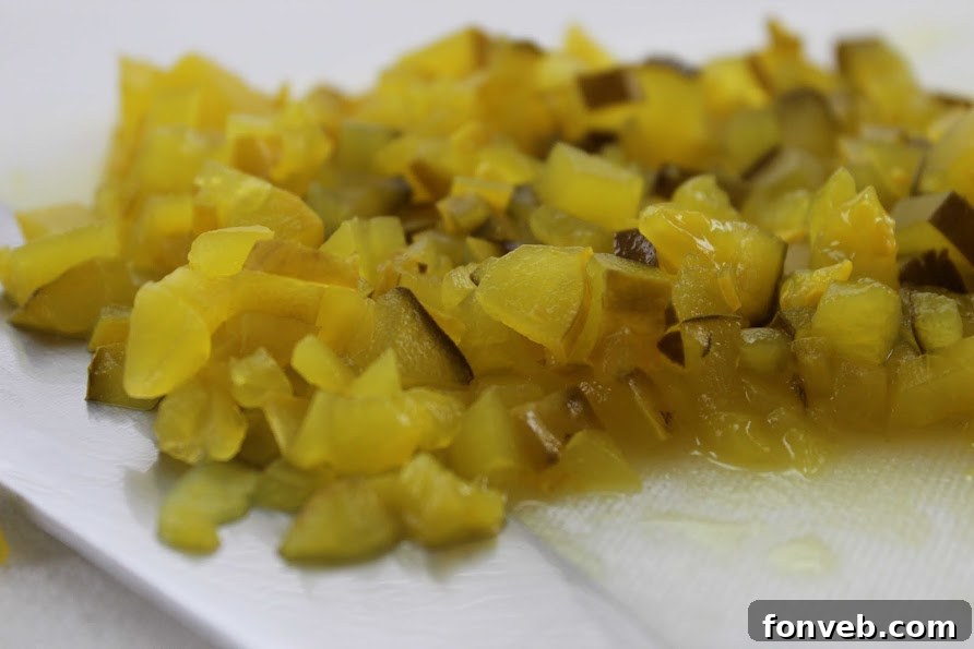 A hand reaching for a potato chip to dip into a bowl of creamy homemade Dill Pickle Dip.