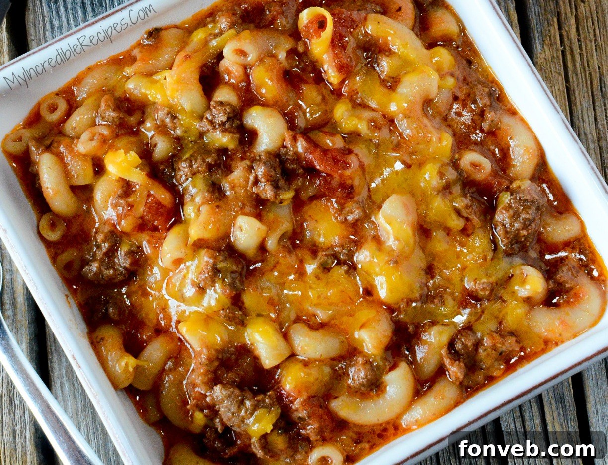 A bowl of Old Fashioned Goulash on a wooden table, steam rising, highlighting its comforting warmth.