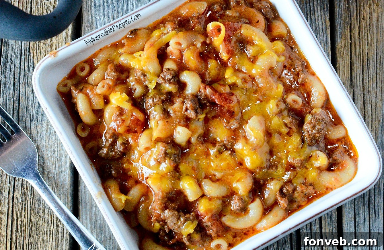 Old Fashioned Goulash served in a white square bowl on a wooden table, with steam rising.