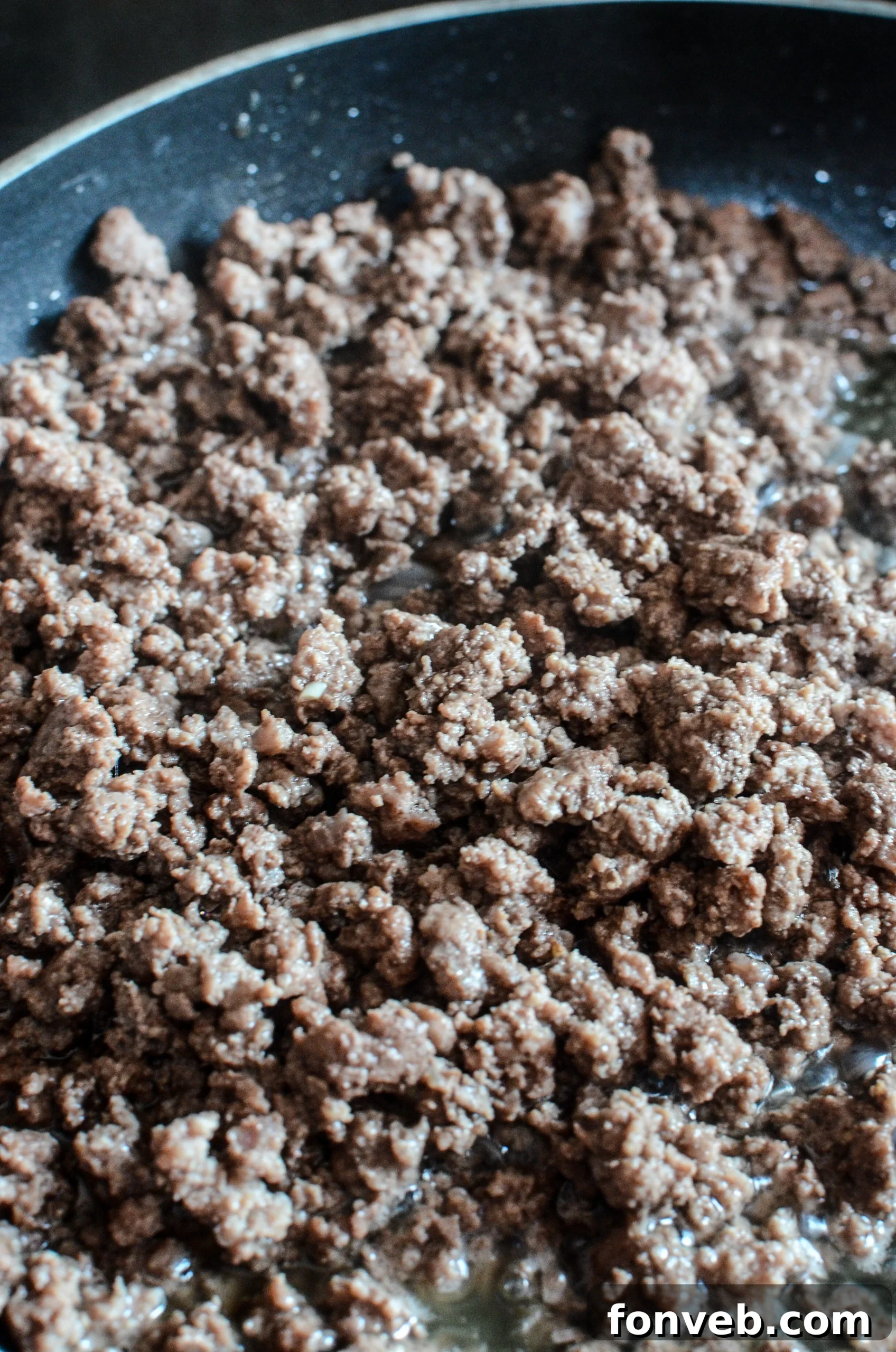 Ground beef and chopped onions sizzling in a large pan, cooking down before the sauce is added.