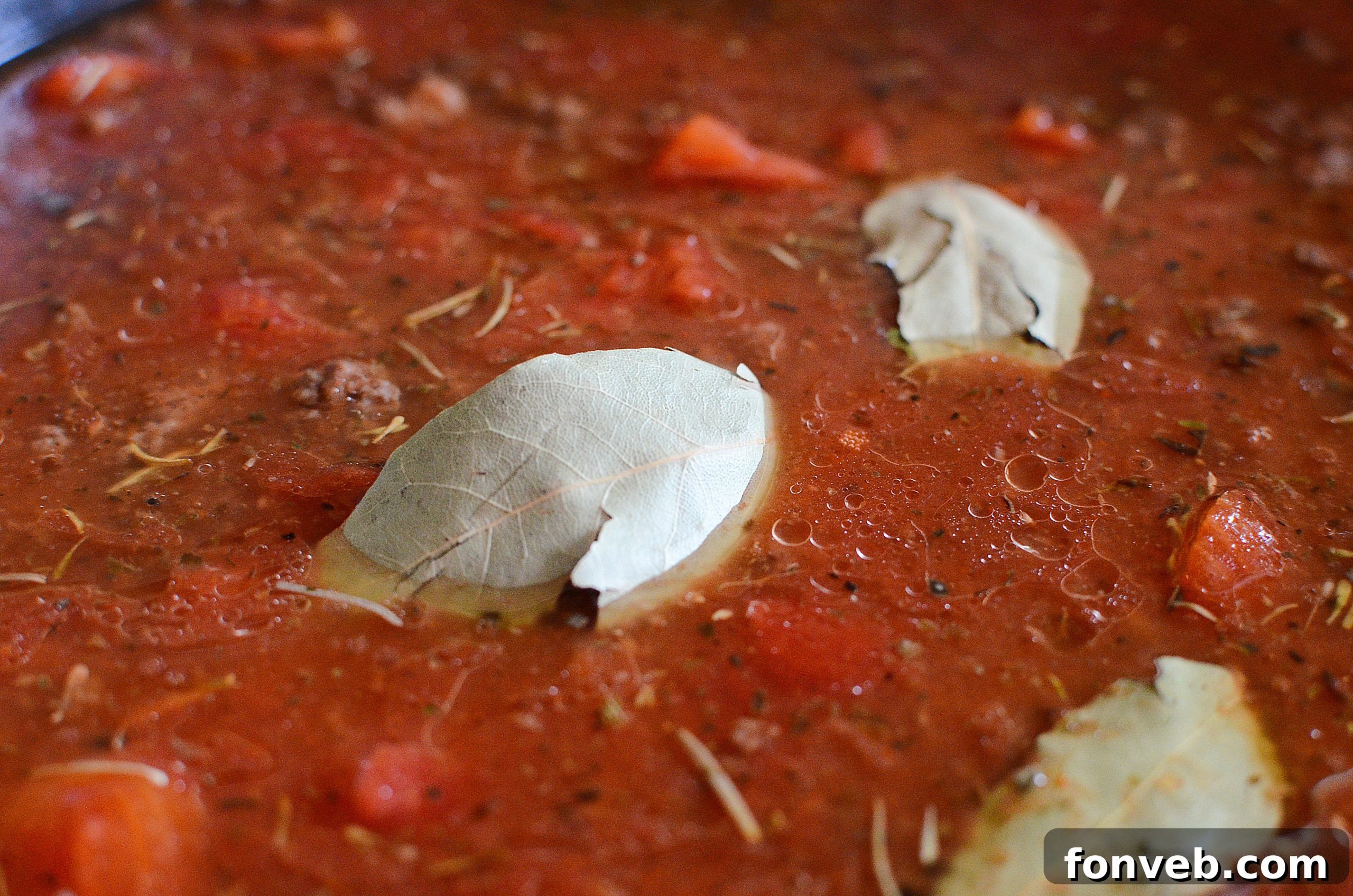 Old Fashioned Goulash simmering in a large pot, with bay leaves visible, releasing a rich aroma.
