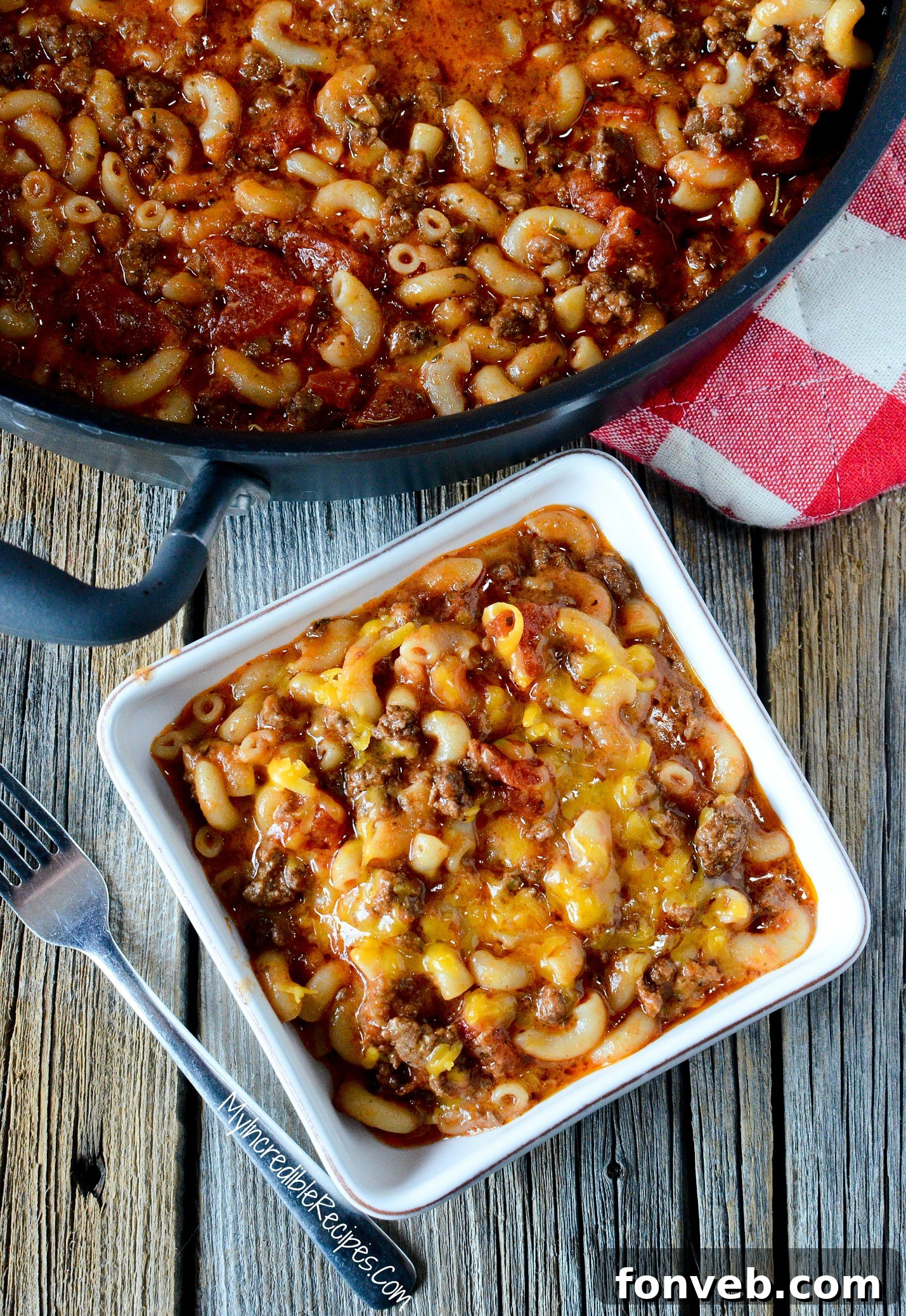 Old Fashioned Goulash in a rustic pot, with a white bowl of goulash topped with cheese on the side, ready to be served.