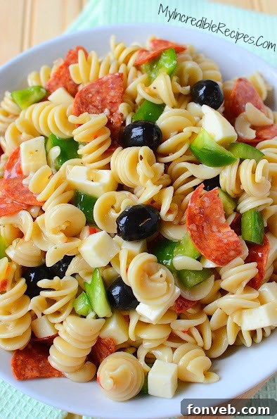 A close-up shot of the dressing being mixed into the Italian Pizza Pasta Salad, showing the glistening pasta and ingredients