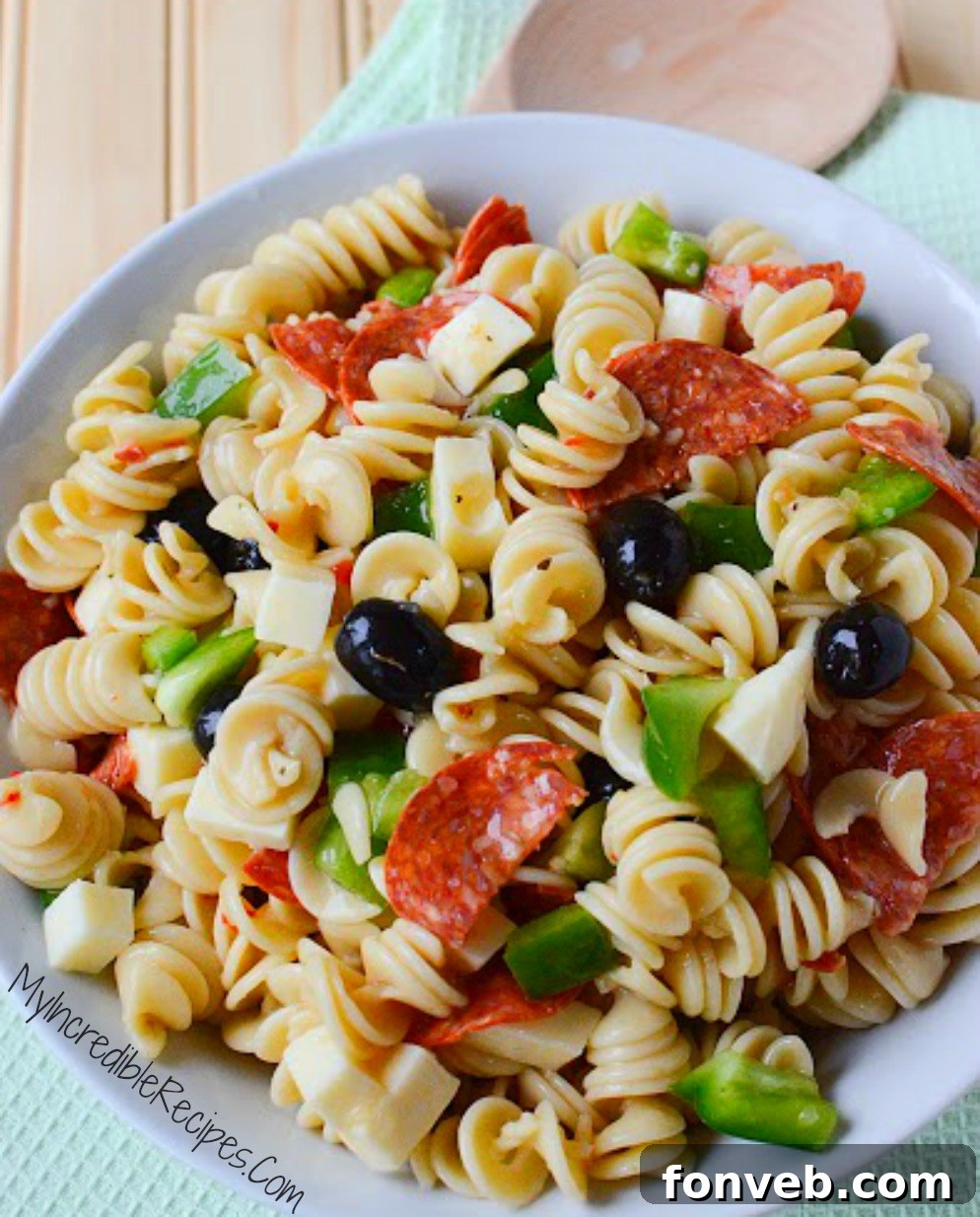 A hand mixing a large bowl of Italian Pizza Pasta Salad, emphasizing the freshly combined ingredients before chilling