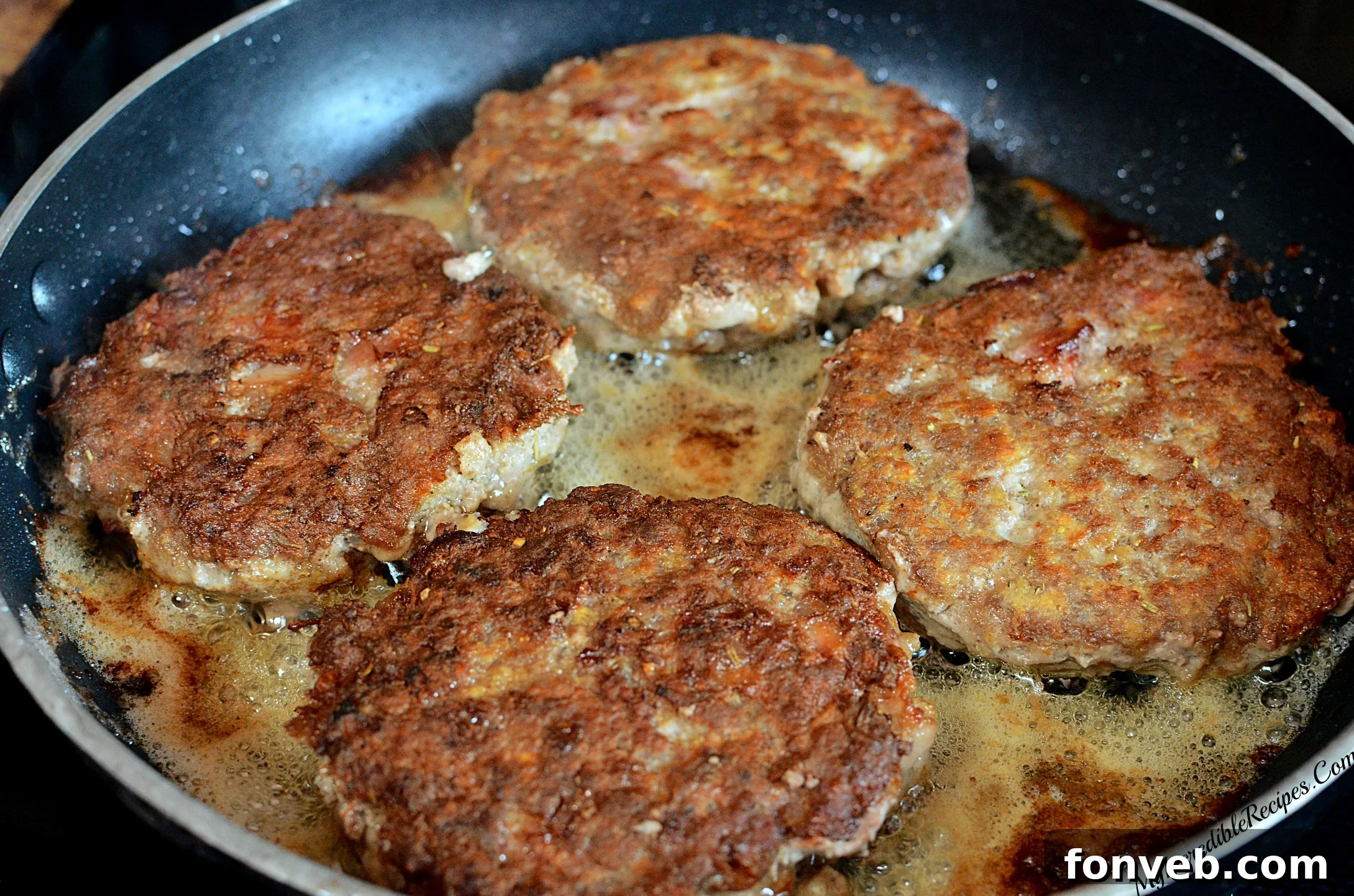 Hamburger steak patties sizzling in a hot skillet, creating savory pan drippings.
