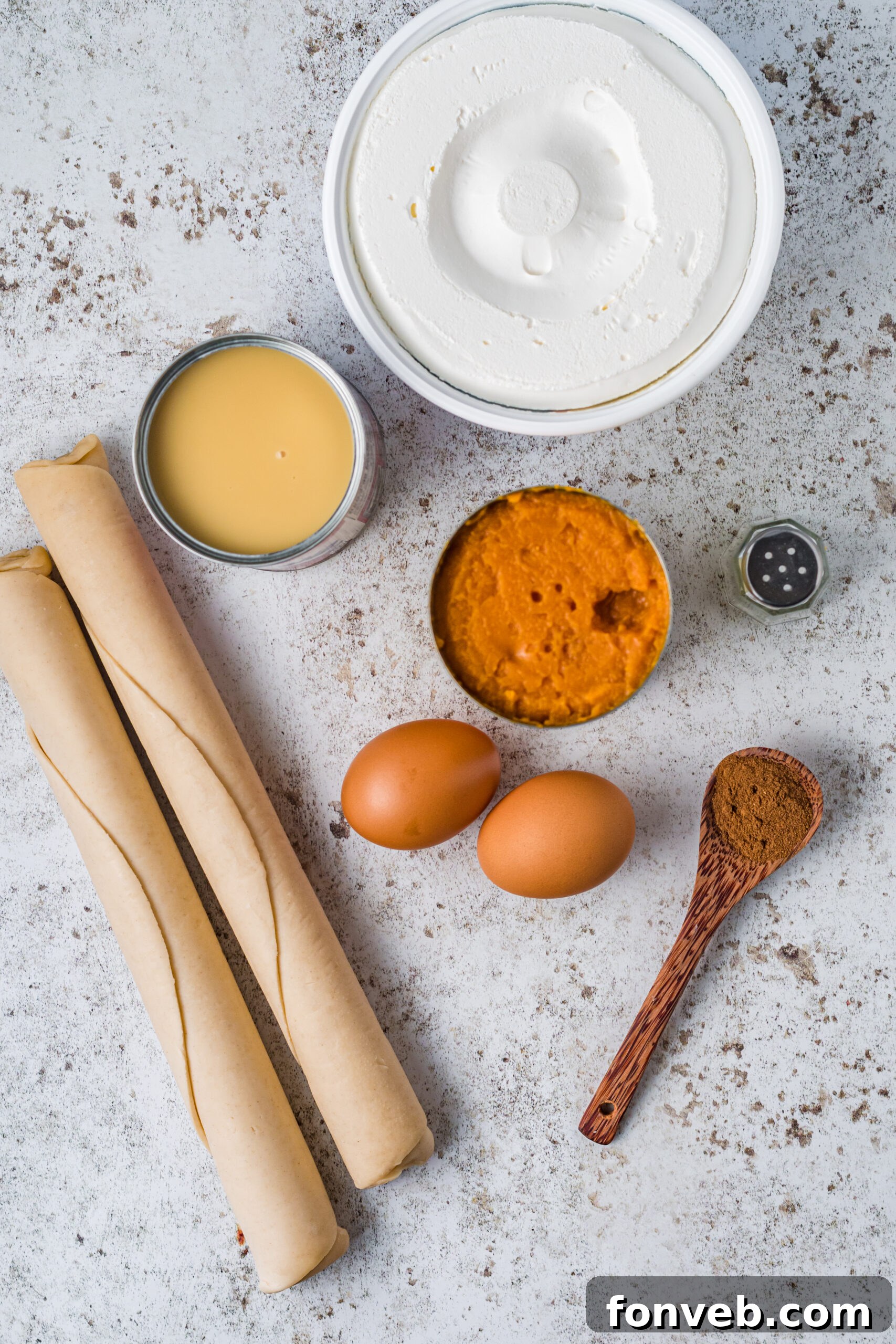 Ingredients laid out for making mini pumpkin pies: pie crust, pumpkin puree, sweetened condensed milk, eggs, pumpkin spice, salt, and Cool Whip