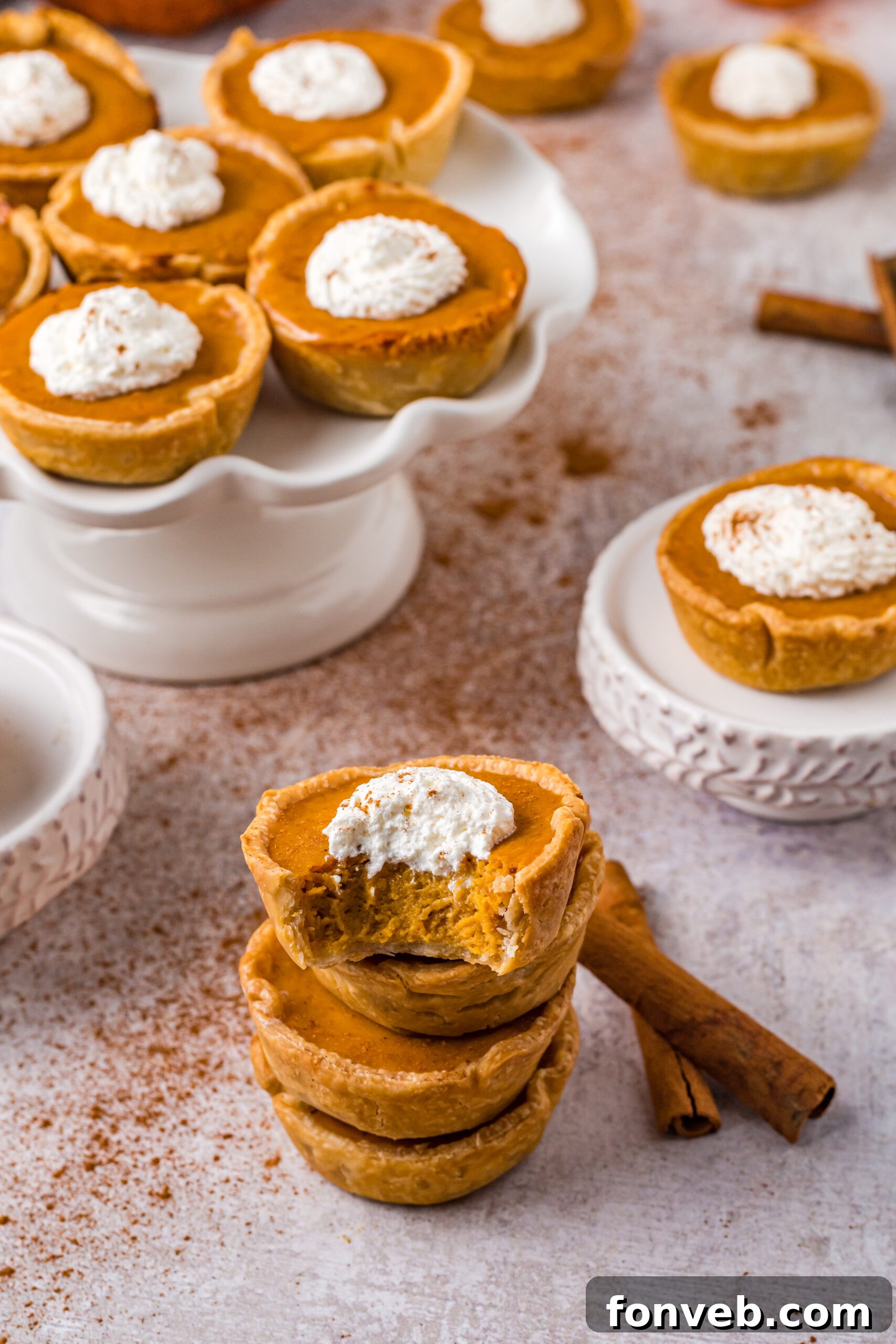 Mini Pumpkin Pies stacked with a bite missing and topped with whipped cream, showing off the creamy filling