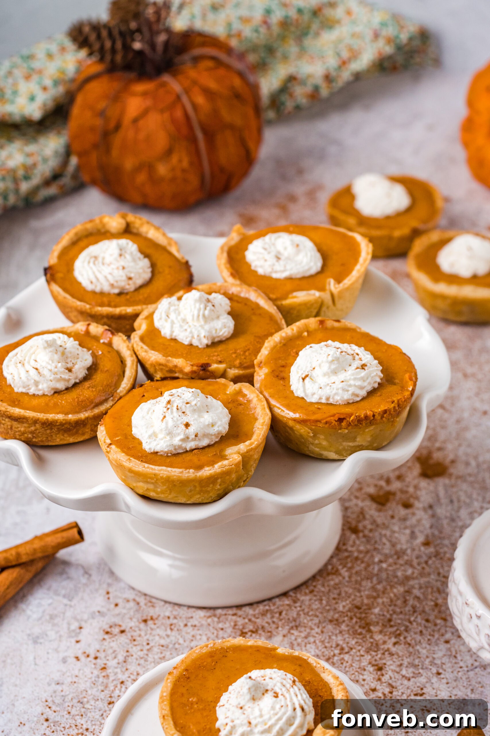 Mini Pumpkin Pies on a white cake stand, all generously topped with dollops of whipped cream