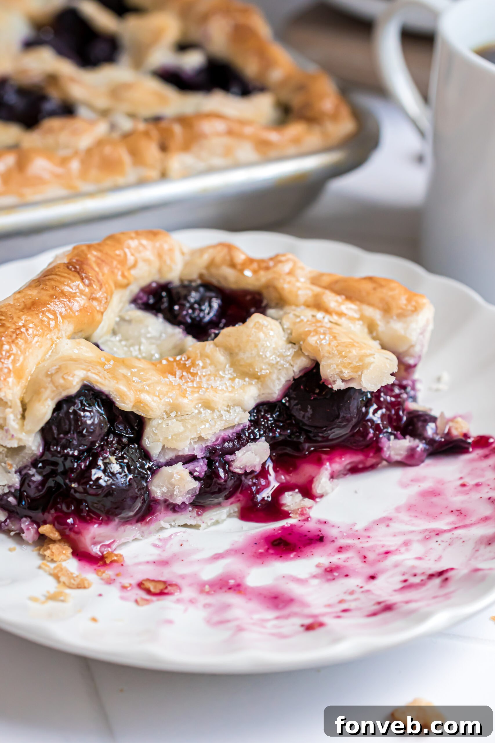 A tempting slice of Blueberry Slab Pie on a white plate, with a few bites already savored, revealing the luscious blueberry filling.