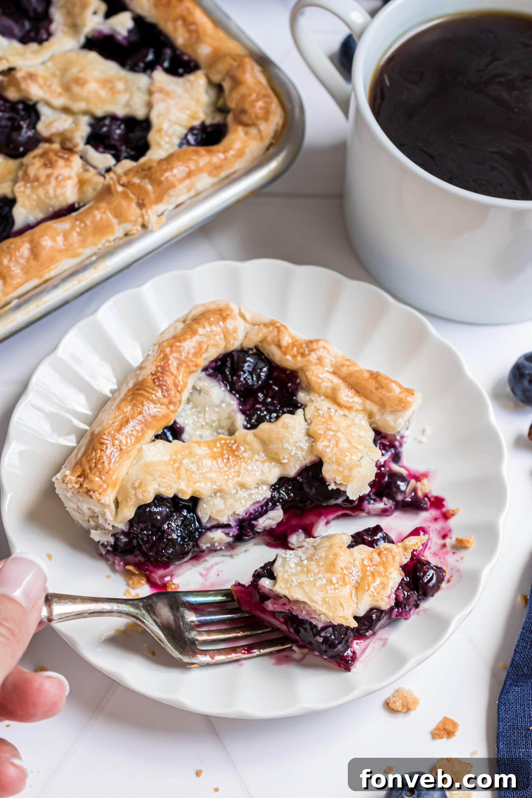 A delicious slice of Blueberry Slab Pie on a white plate, with a fork poised to take a delightful bite.