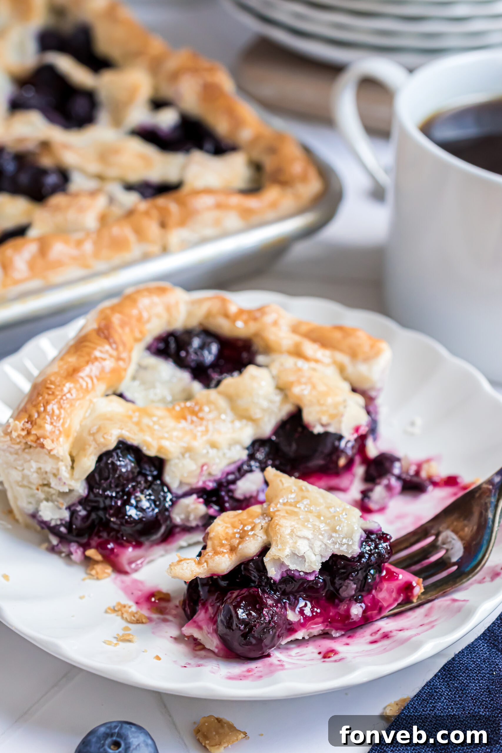 A delectable slice of Blueberry Slab Pie resting on a white plate, with a fork poised to scoop up a mouthwatering bite.